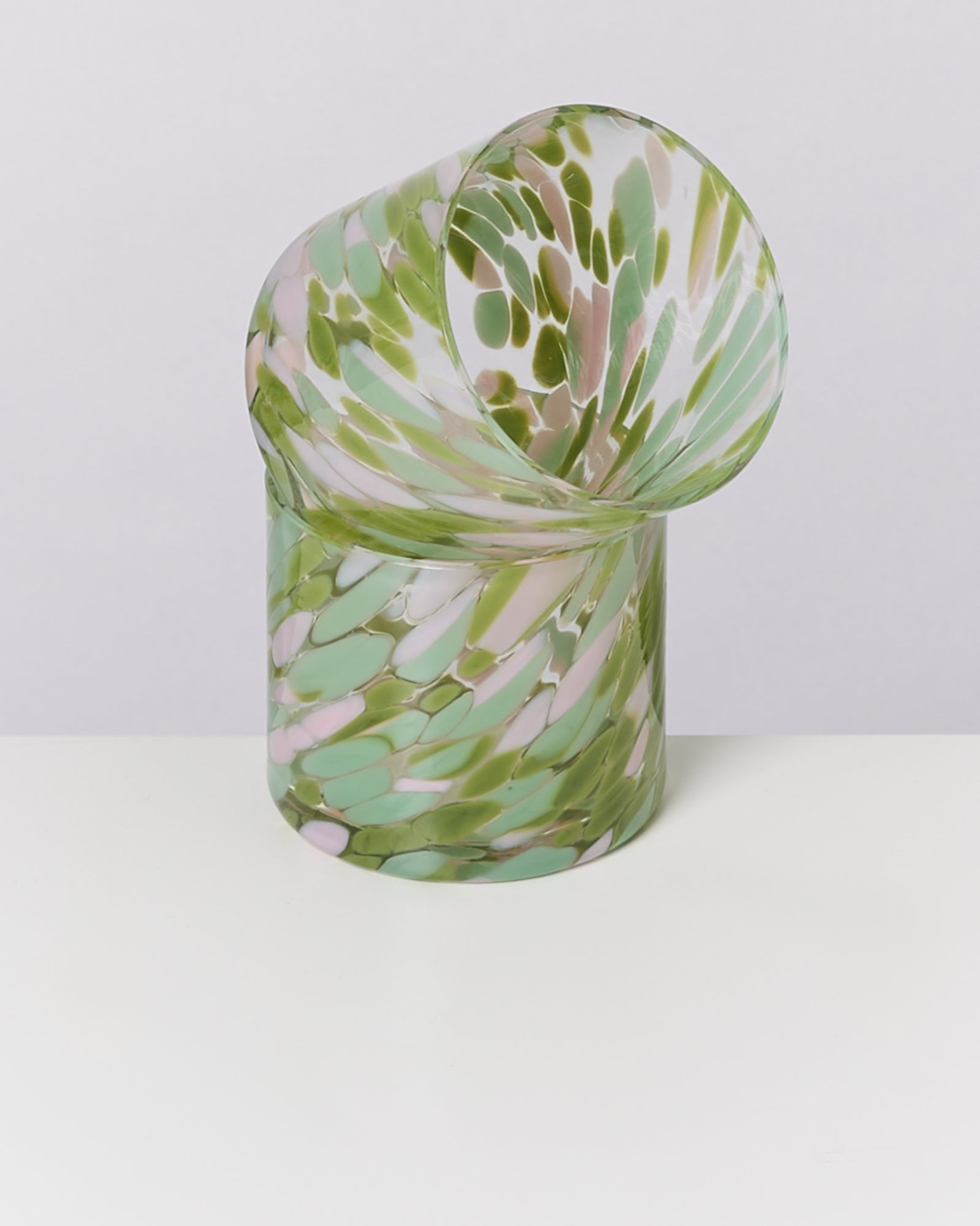 Abstrakte Glasvase mit grün-rosa Marmorierung auf weißer Oberfläche vor grauem Hintergrund.