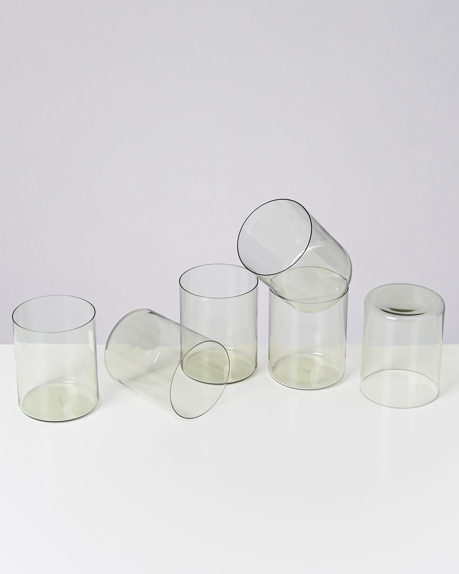Fünf durchsichtige Gläser, von denen drei stehen und zwei liegen, auf weißem Hintergrund.