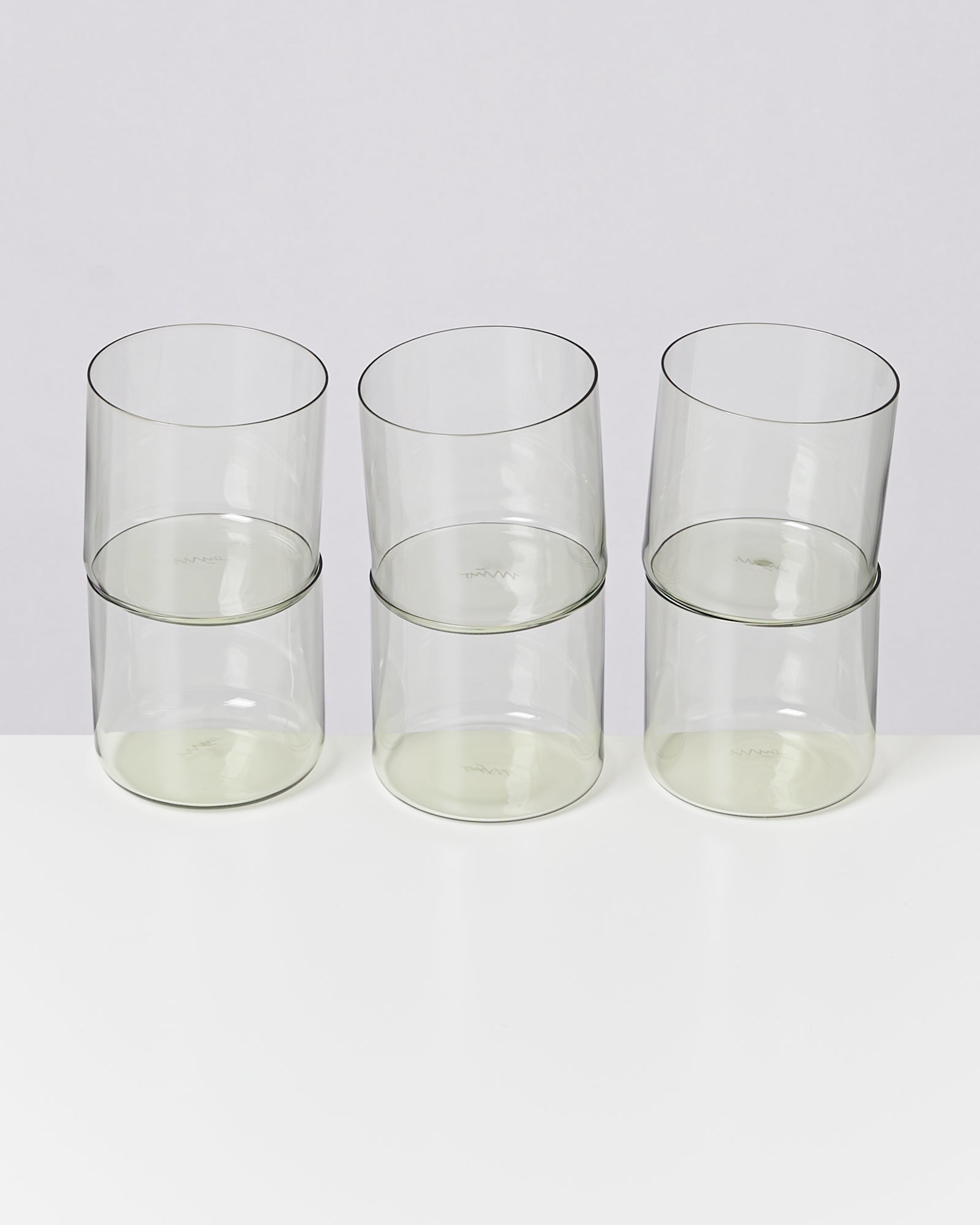 Sechs gestapelte Gläser auf einem weißen Tisch vor einem hellgrauen Hintergrund.