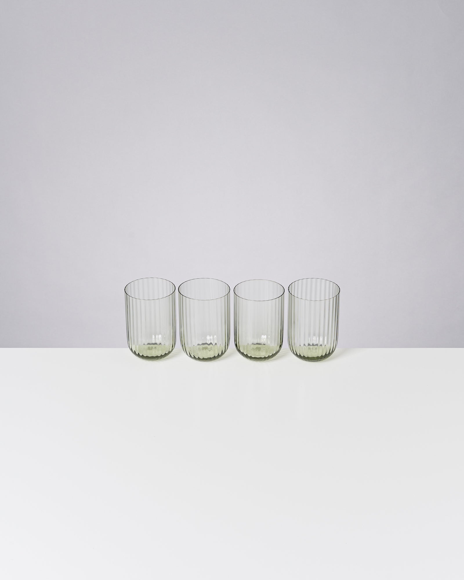 Vier geriffelte Gläser stehen nebeneinander auf einem weißen Tisch vor einem grauen Hintergrund.