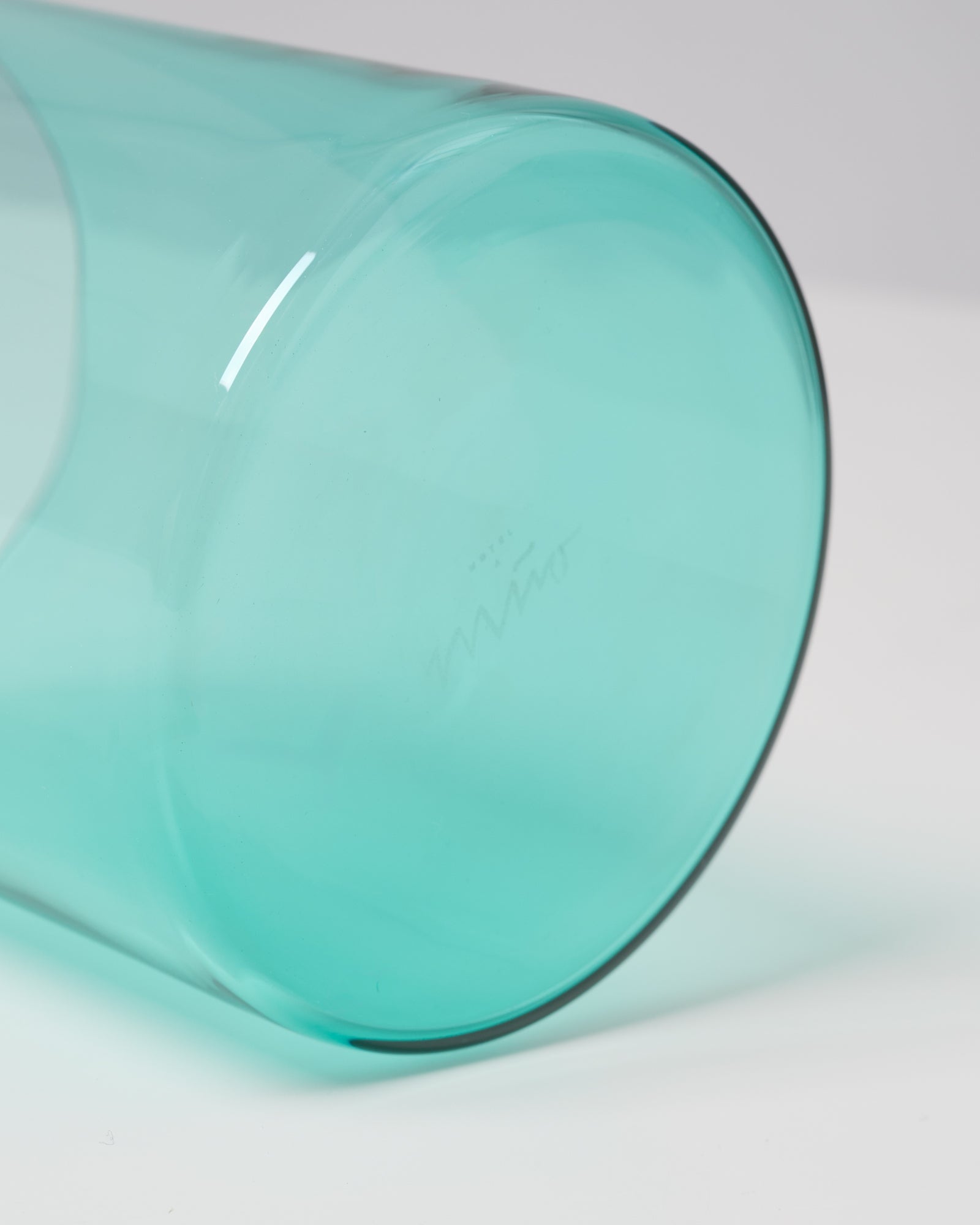 Nahaufnahme eines umgestürzten, türkisfarbenen Glases auf einer weißen Oberfläche.