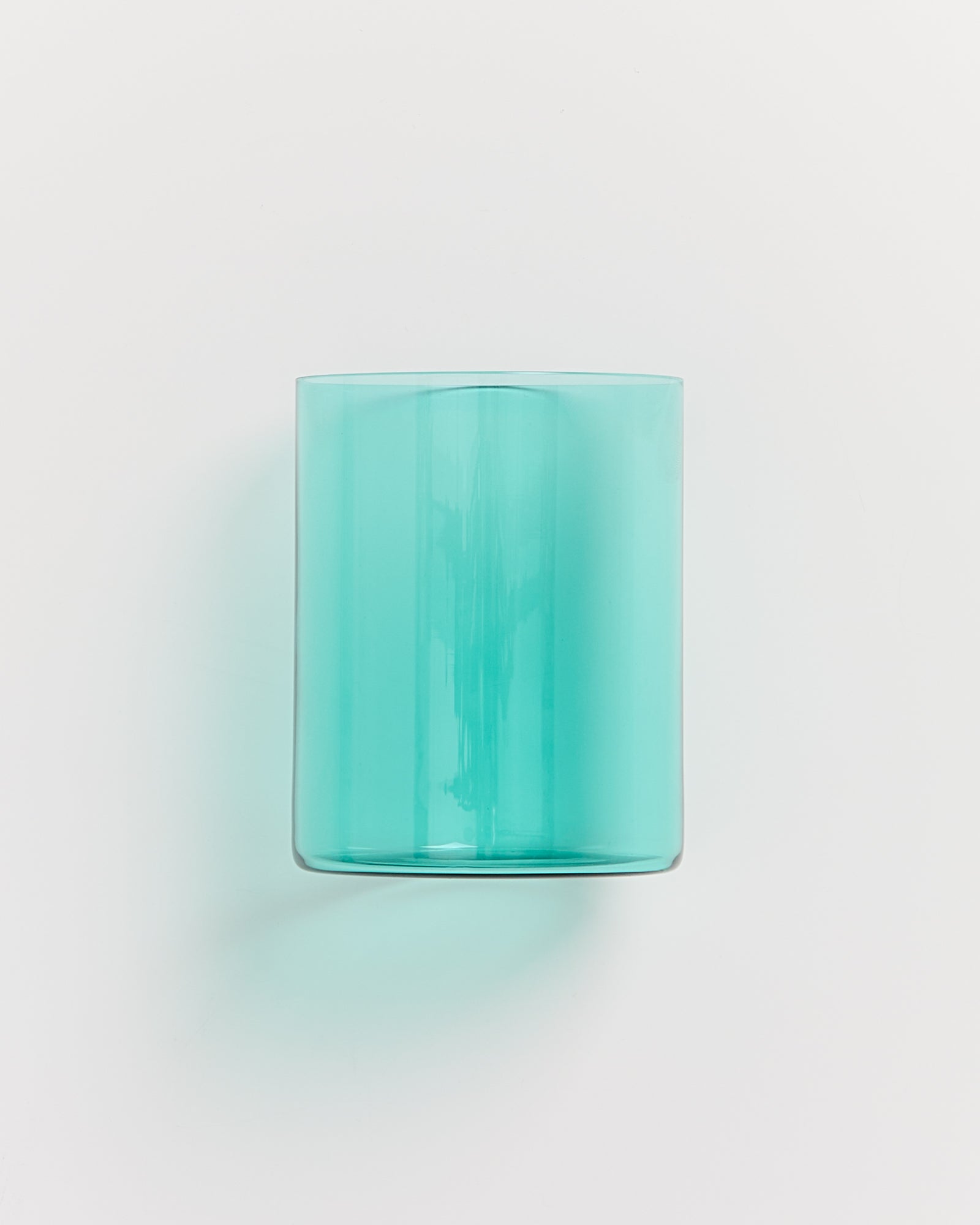 Ein transparentes, türkisfarbenes Glas mit abgerundeten Kanten steht aufrecht vor einem weißen Hintergrund.