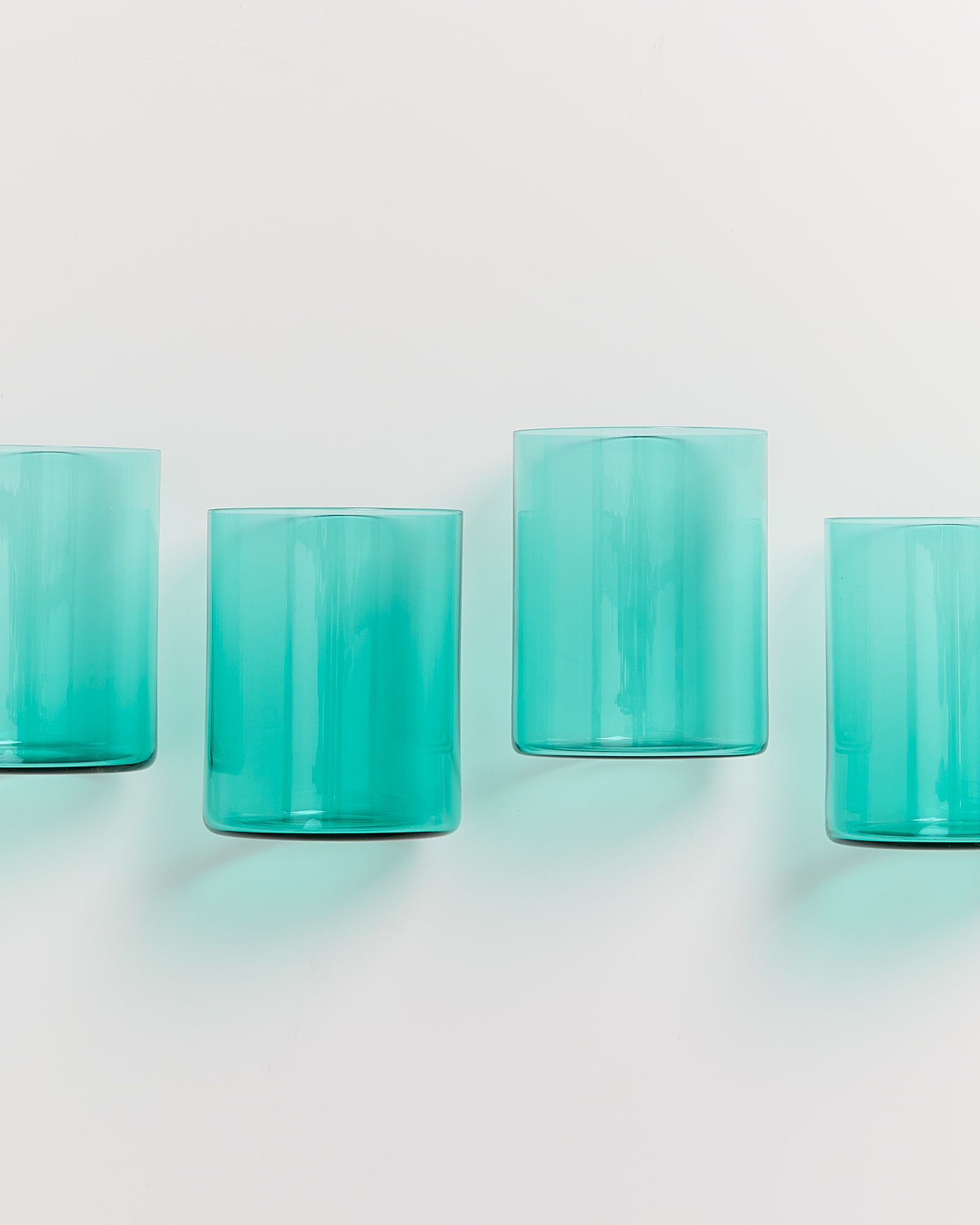 Vier türkisfarbene Gläser stehen in einer Reihe auf einem weißen Hintergrund.