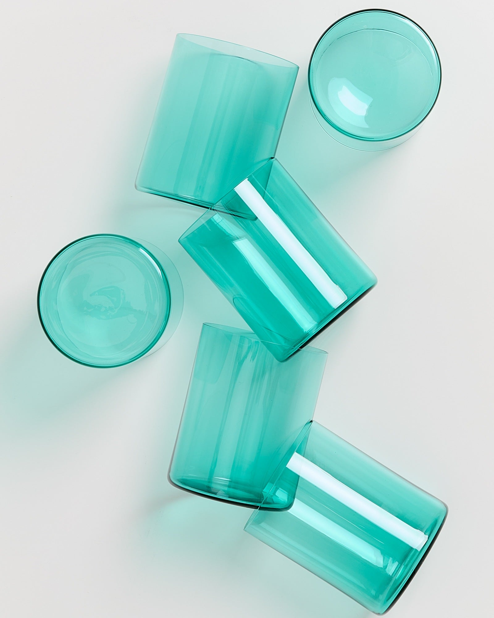Fünf türkisfarbene Gläser liegen verstreut auf einer weißen Oberfläche.