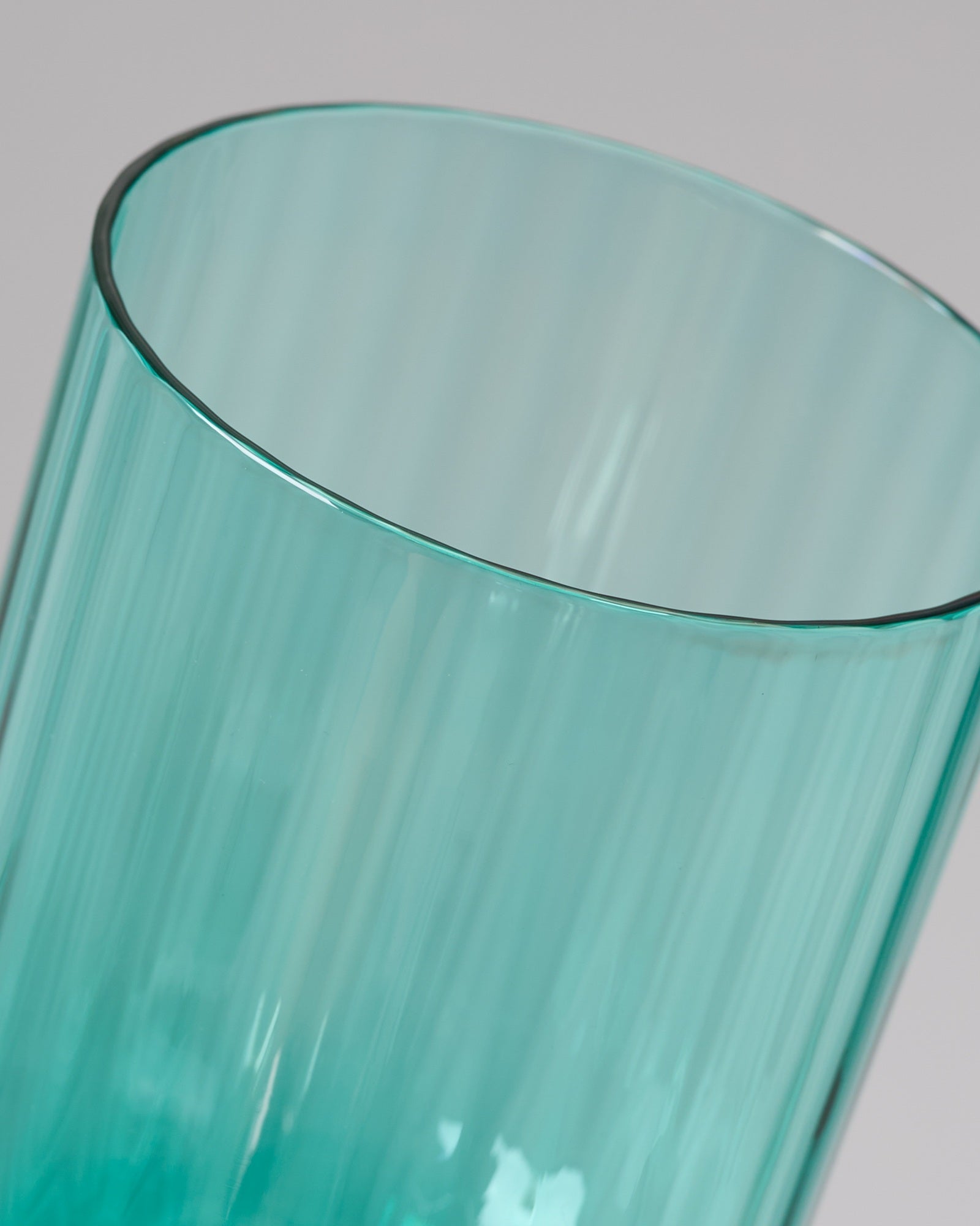 Nahaufnahme eines türkisfarbenen, geriffelten Trinkglases auf grauem Hintergrund.