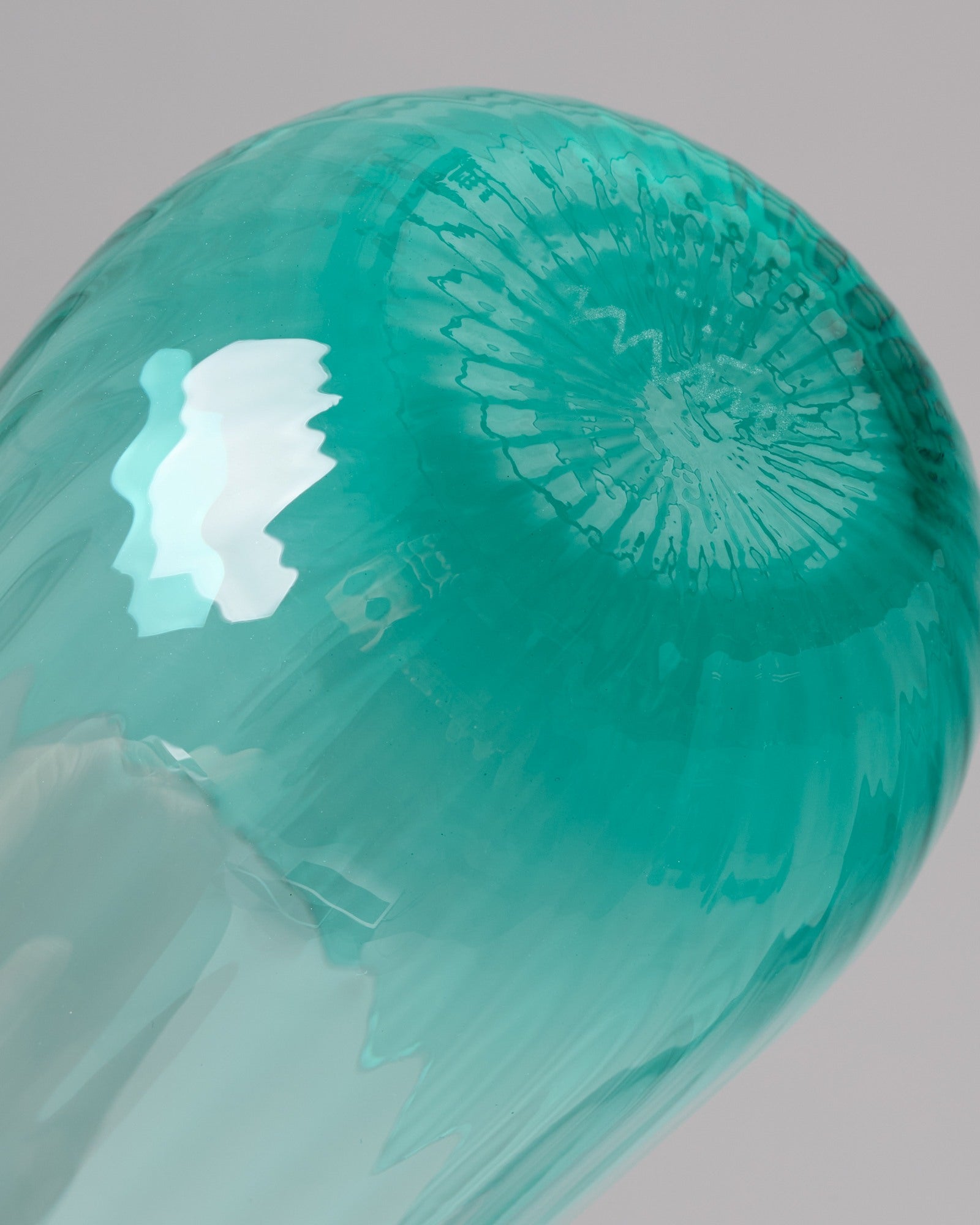 Nahaufnahme eines türkisfarbenen Glasobjekts mit konzentrischen Mustern und glänzender Oberfläche.