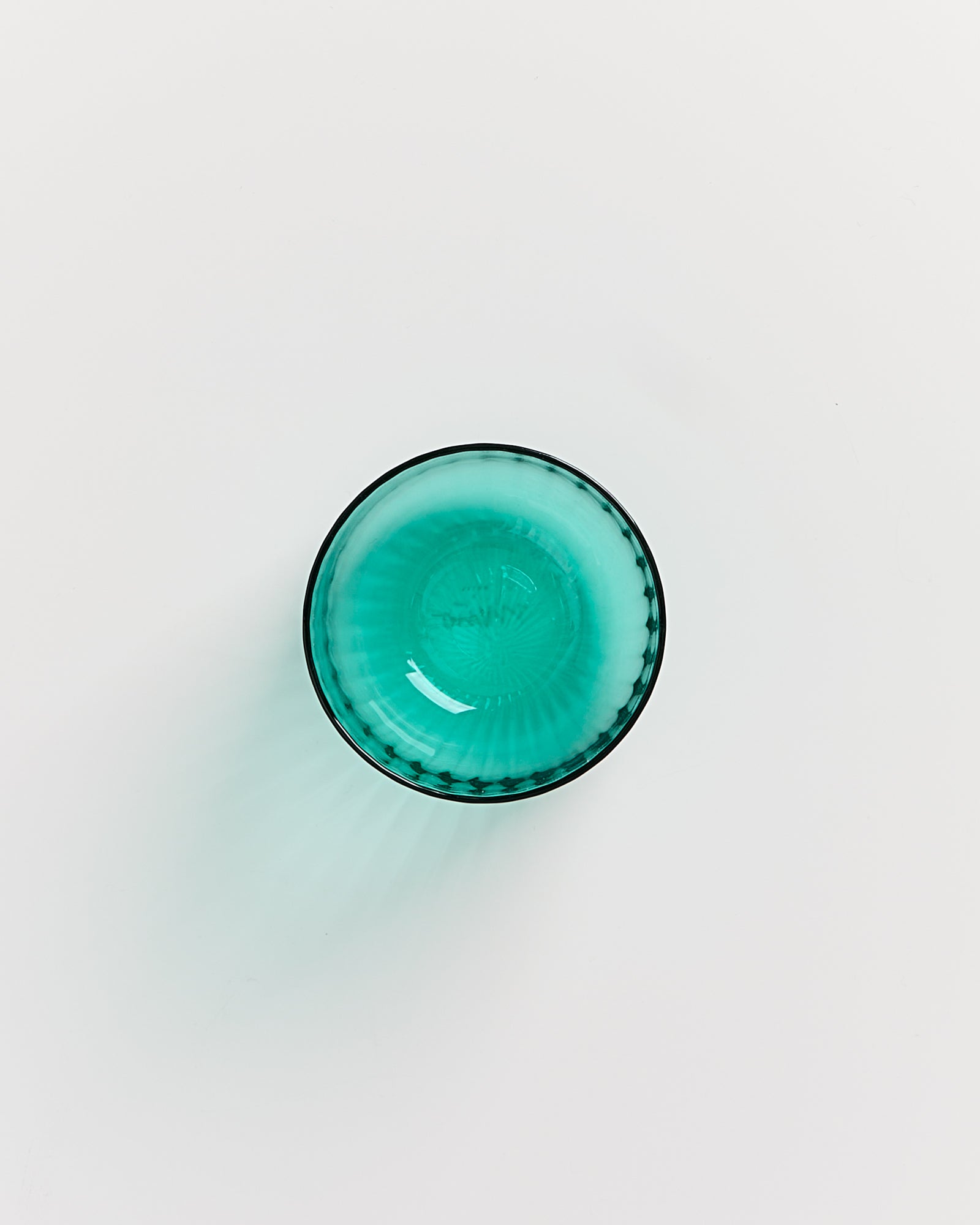 Runde, türkisfarbene Glasschale auf weißem Hintergrund von oben betrachtet.