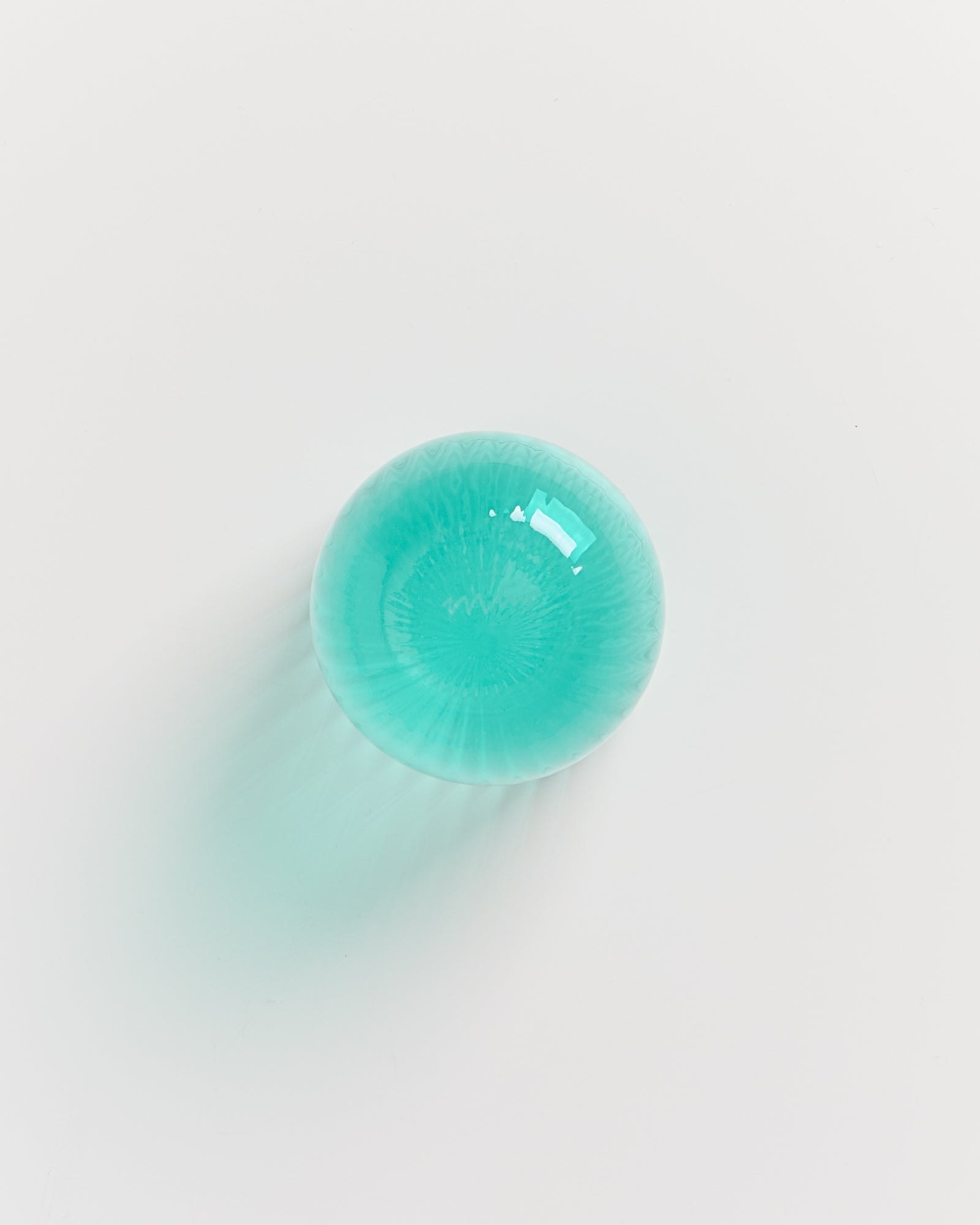 Runde, türkisfarbene Glaslinse auf weißem Hintergrund, die einen Schatten wirft.