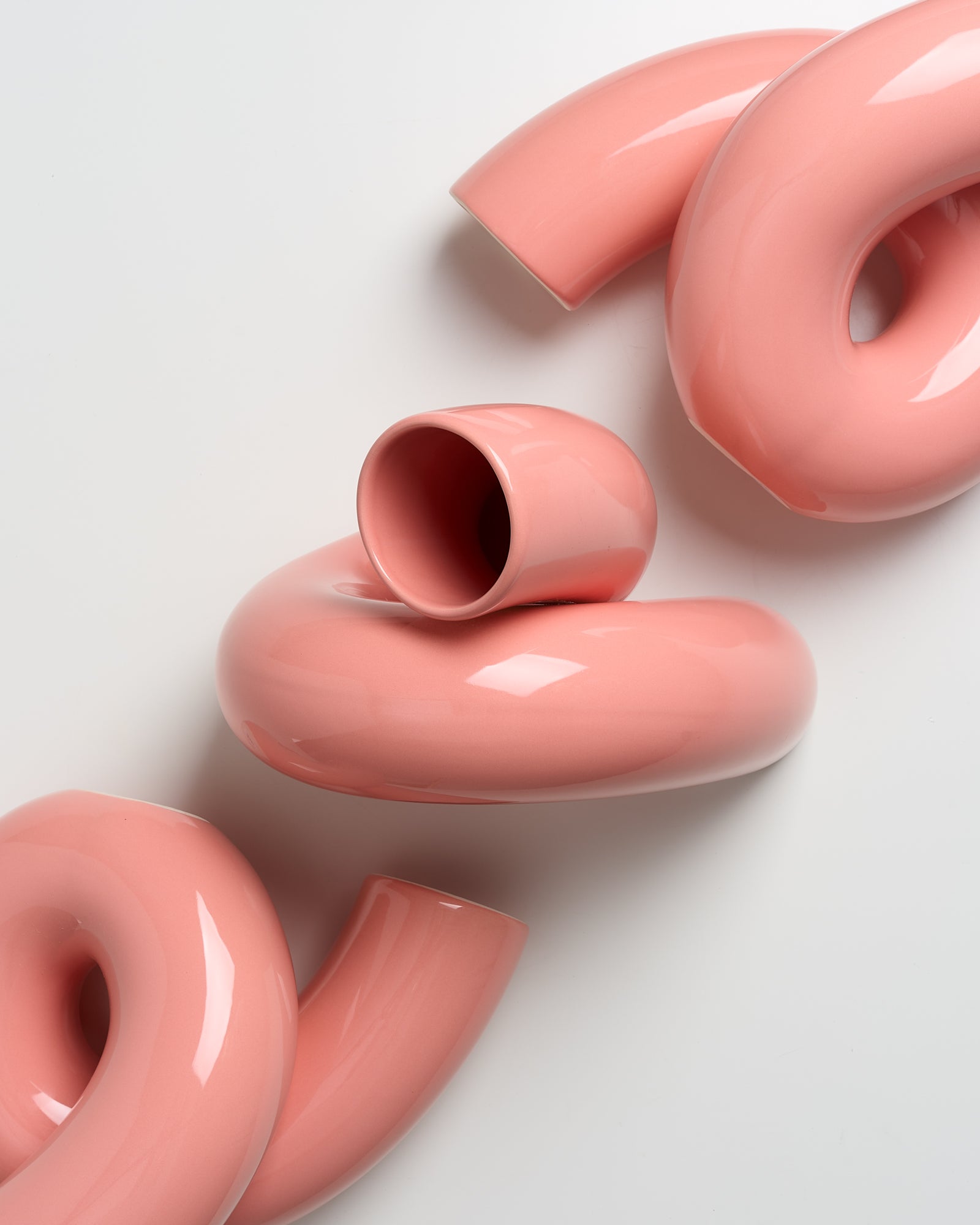 Rosa, geschwungene Keramikvasen mit glatter Oberfläche liegen auf einer weißen Fläche.