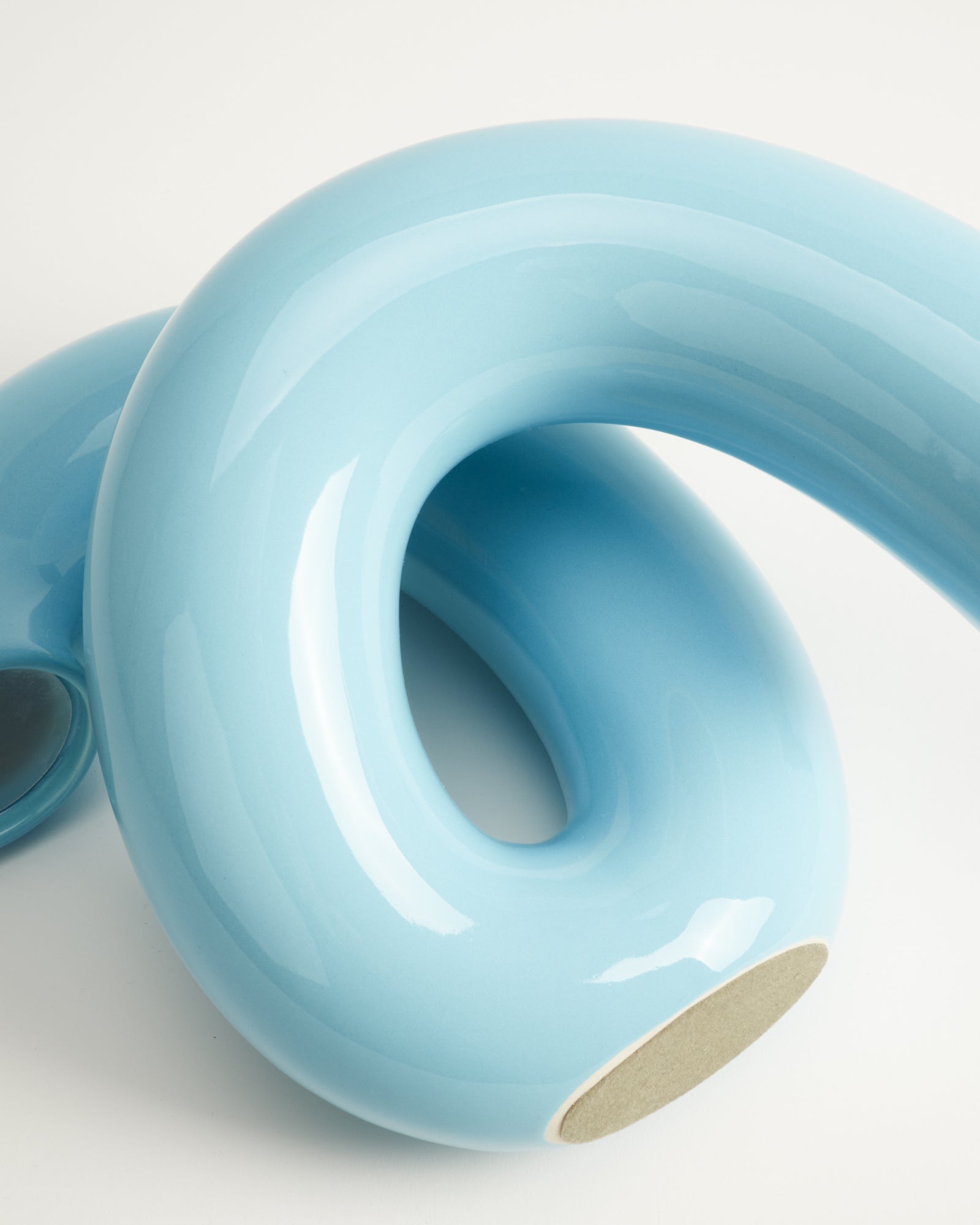 Hellblaues, gebogenes Keramikobjekt mit glänzender Oberfläche auf weißem Hintergrund.