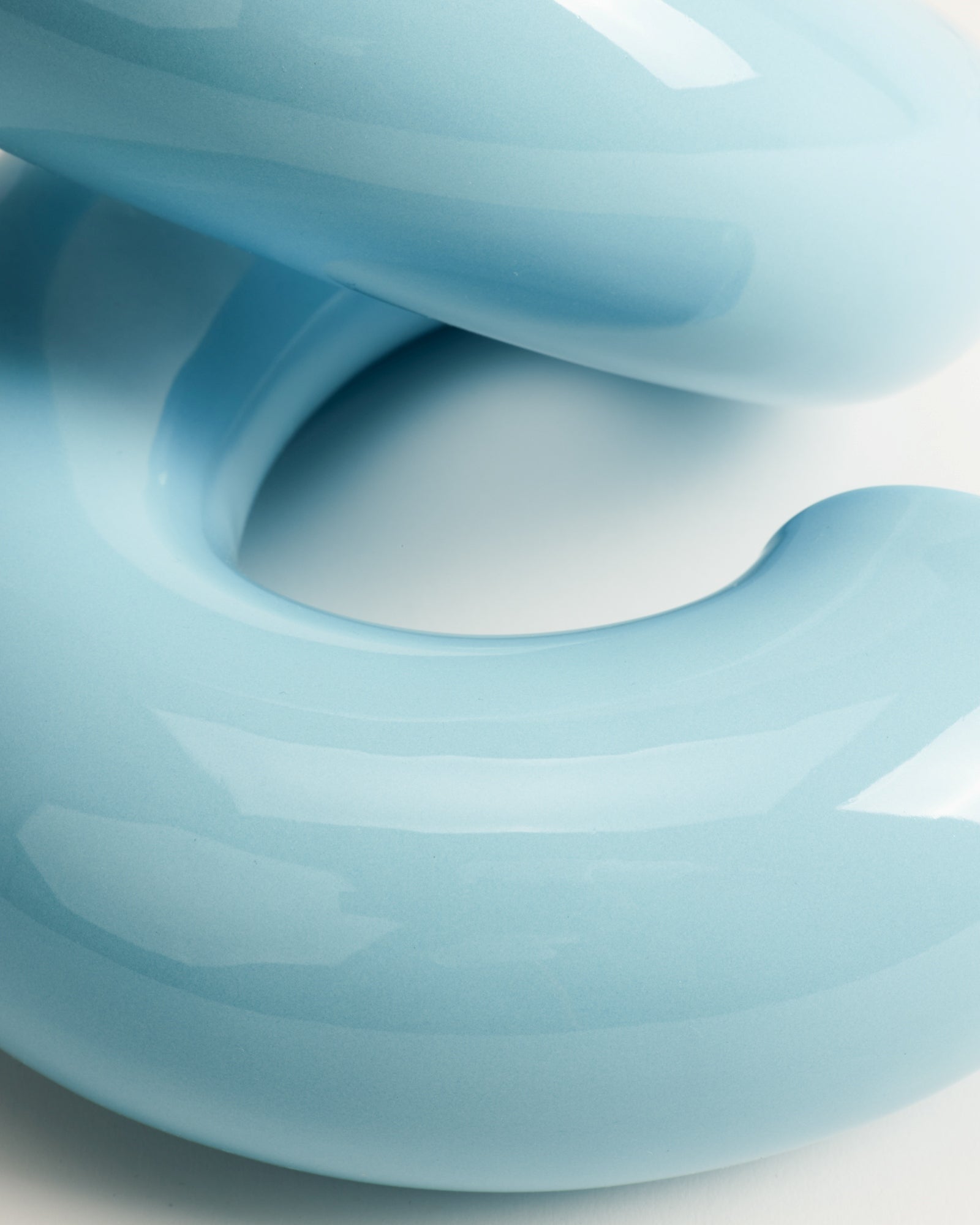 Nahaufnahme einer blauen, glänzenden Skulptur in geschwungener Form vor einem weißen Hintergrund.