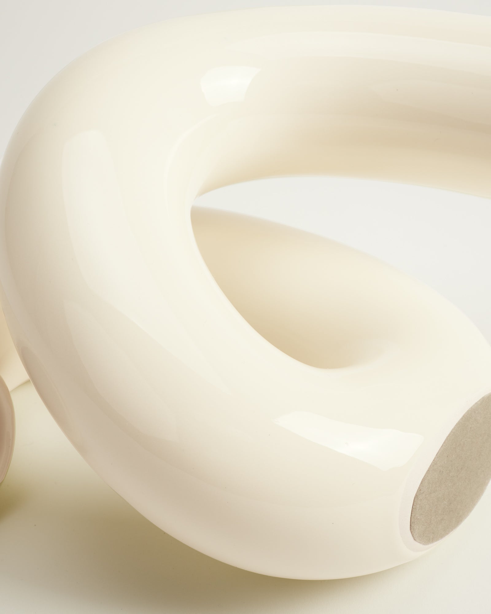 Weißes, glänzendes Kunststoff- oder Keramikobjekt mit geschwungener, röhrenförmiger Form auf hellem Hintergrund.