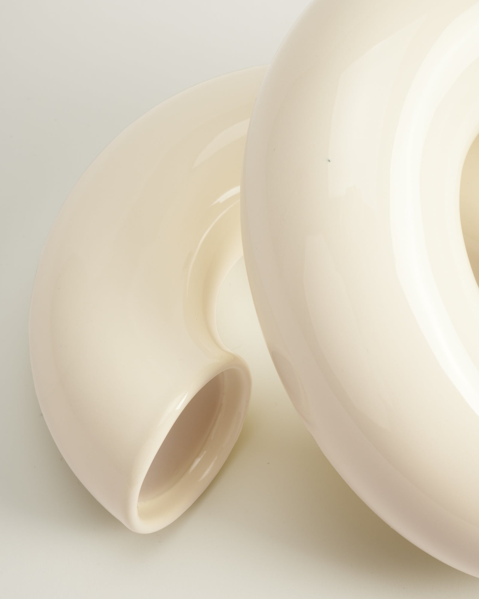 Nahaufnahme von zwei cremefarbenen, gebogenen Keramikobjekten mit glänzender Oberfläche.