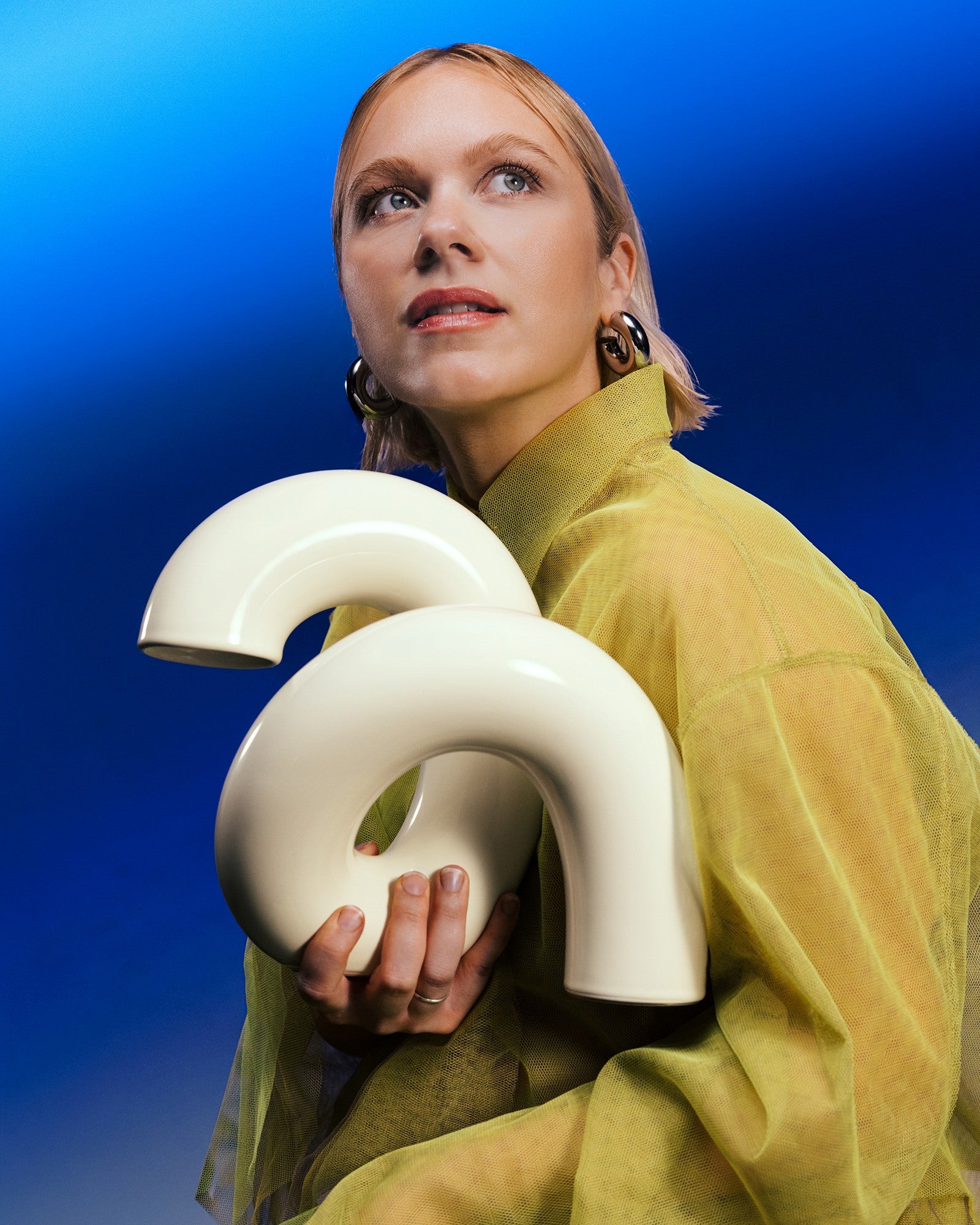 Eine Person in gelber Kleidung hält zwei weiße, gebogene Objekte vor einem blauen Hintergrund.