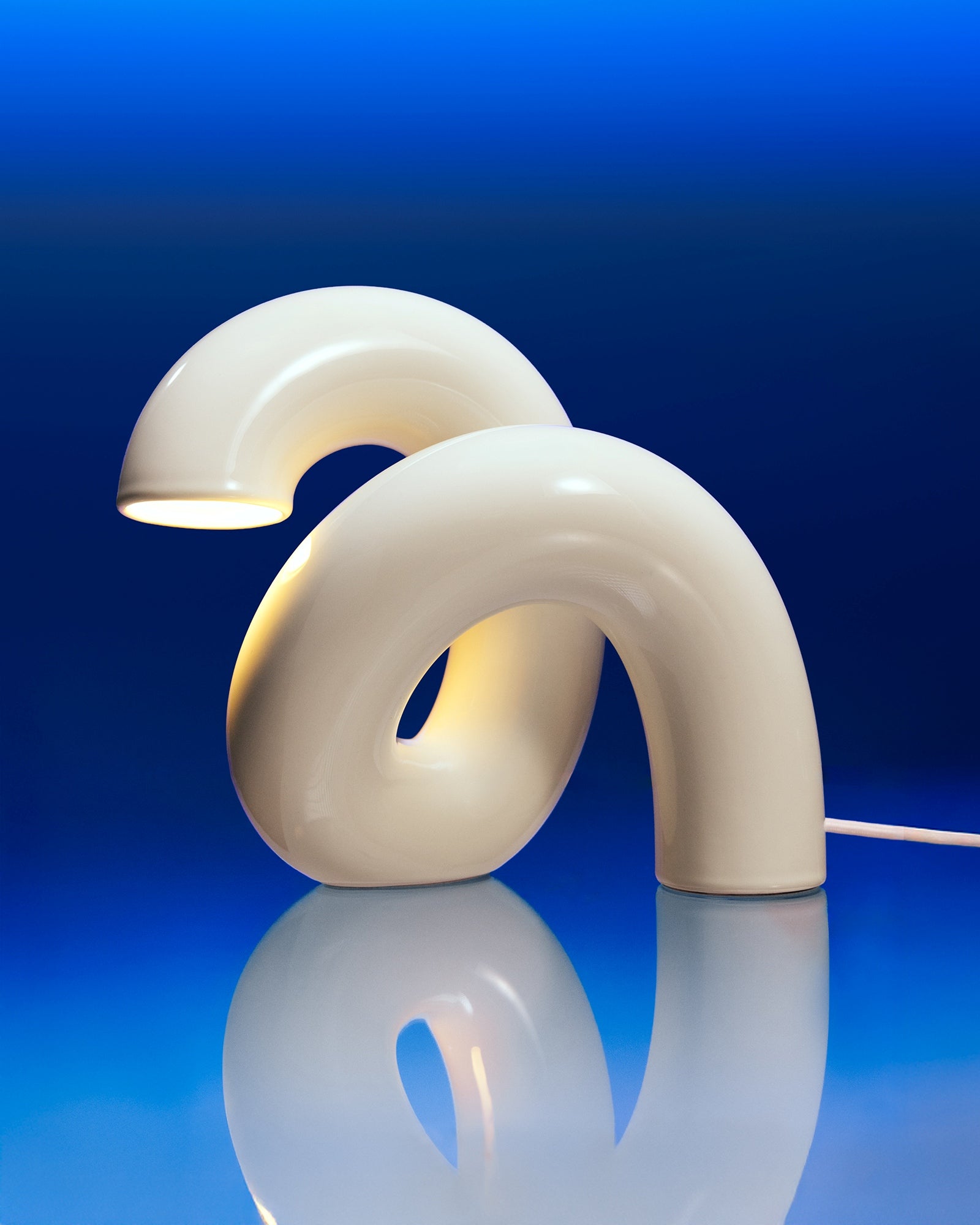 Geschwungene, weiße Tischlampe mit modernem Design vor einem blauen Hintergrund.