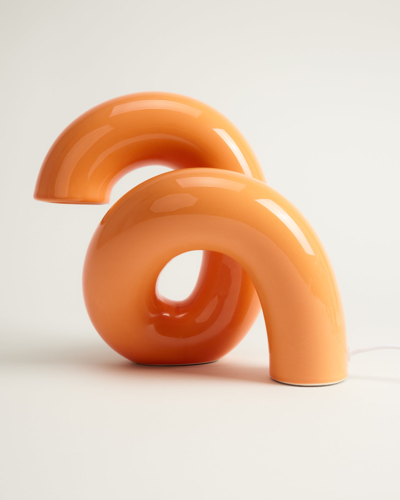 Zwei orange, geschwungene Tischlampen mit glänzender Oberfläche auf weißem Hintergrund.