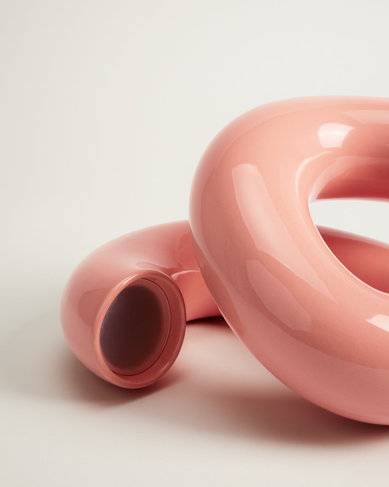 Rosa, glänzende, ineinander verschlungene Röhren auf hellem Hintergrund.