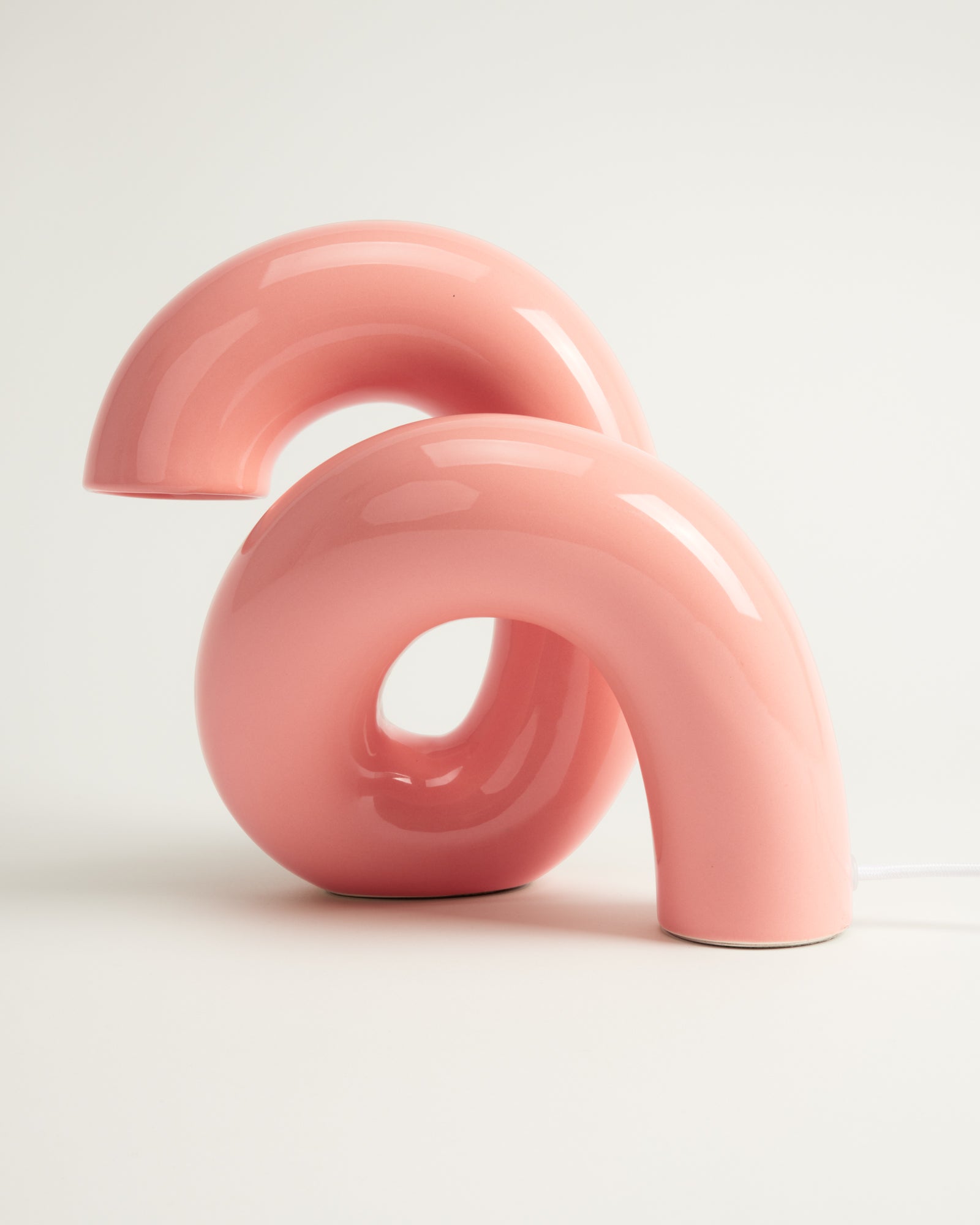 Rosafarbene, moderne Tischlampe in geschwungener Form auf weißem Hintergrund.