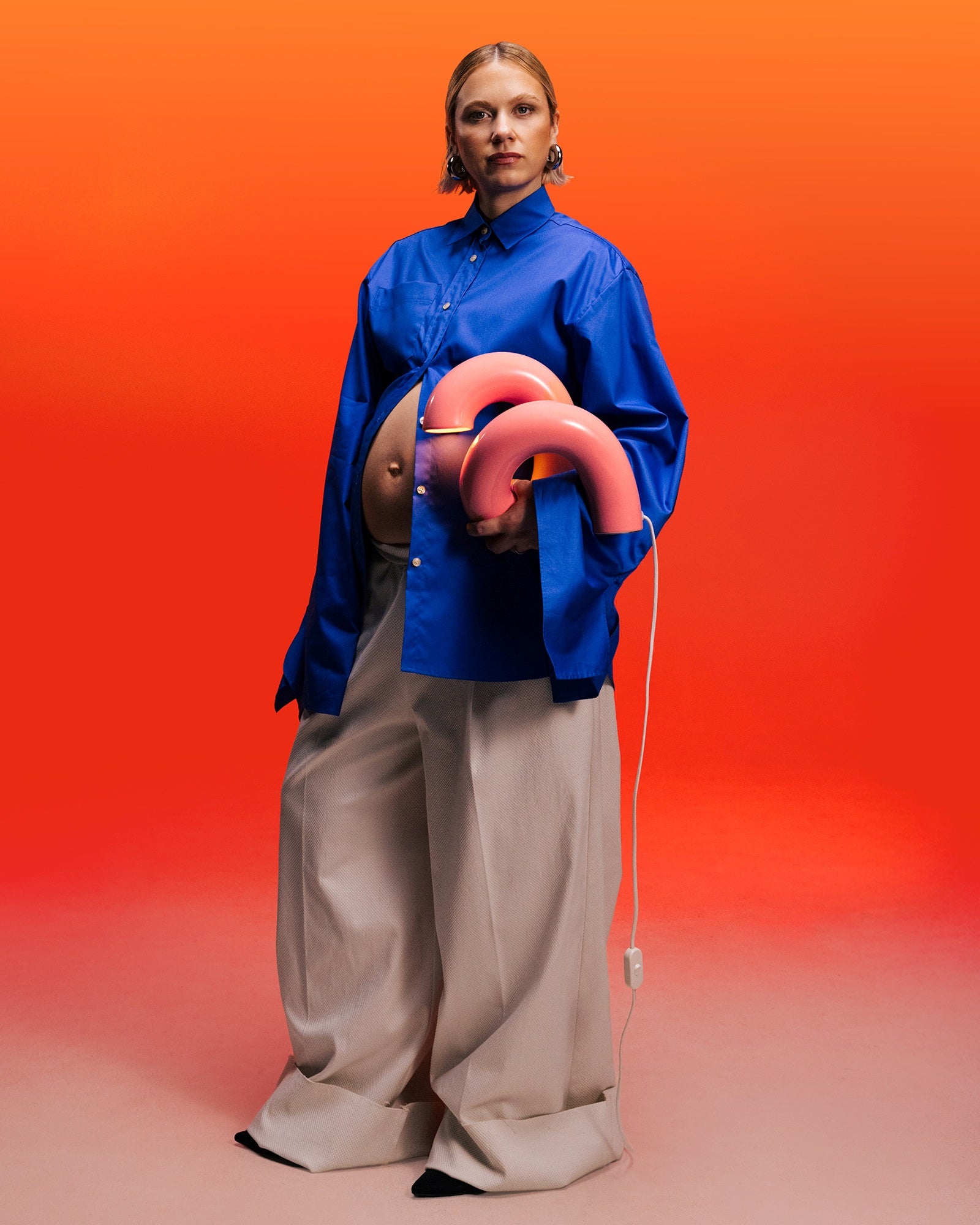 Eine Person in blauer Bluse hält eine pinke Lampe vor einem orangefarbenen Hintergrund.