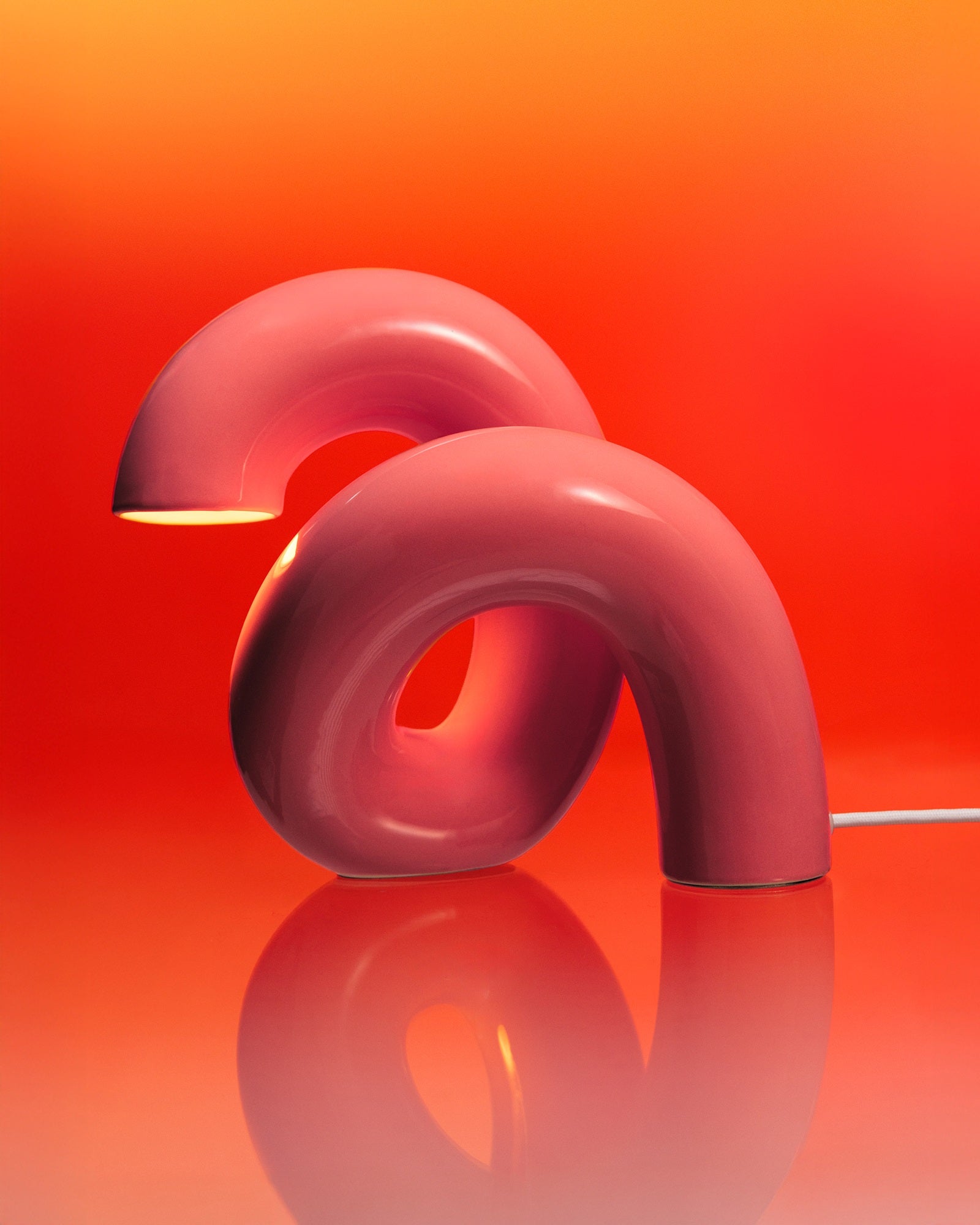 Zwei rosa, gebogene Lampen in modernem Design vor einem warmen, orangefarbenen Hintergrund.