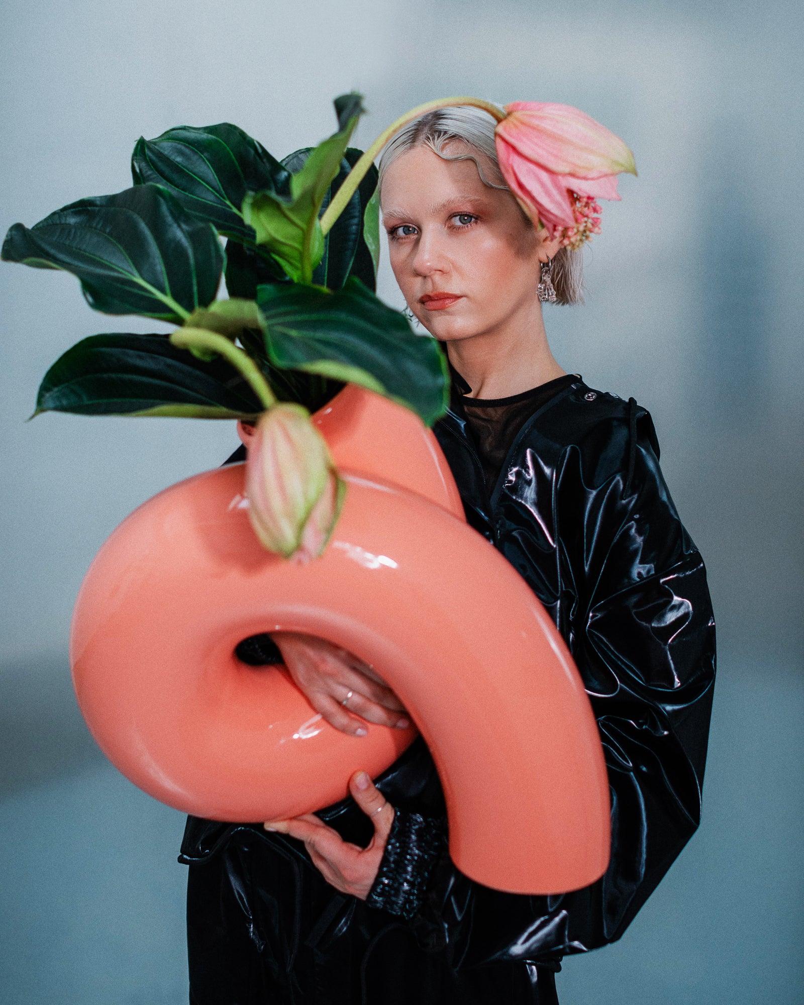 Person in schwarzer Kleidung hält eine große rosa Vase mit grünen Blättern und rosa Blüten.