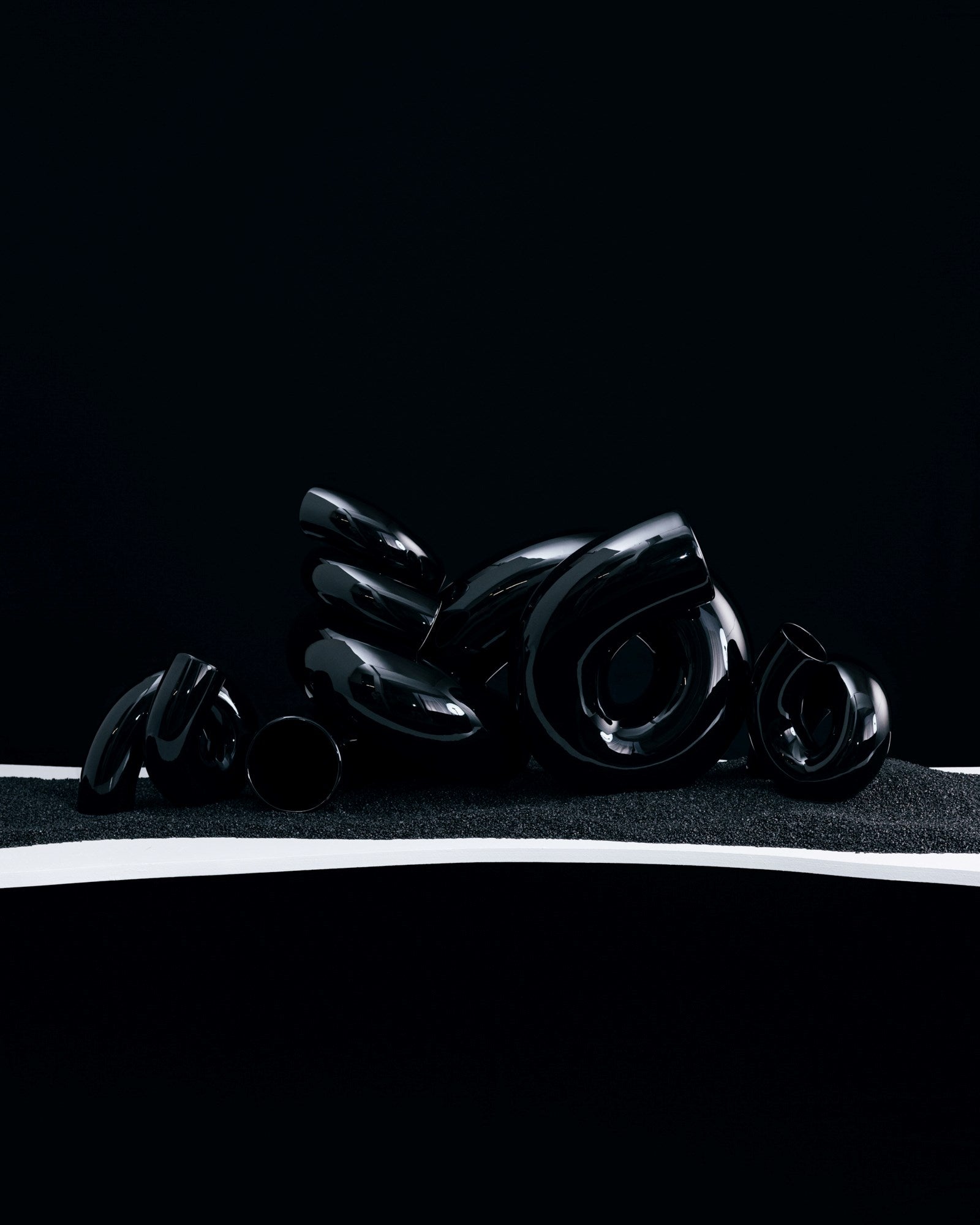 Schwarze, glänzende, abstrakte Skulpturen liegen auf einer dunkel texturierten Oberfläche vor einem schwarzen Hintergrund.