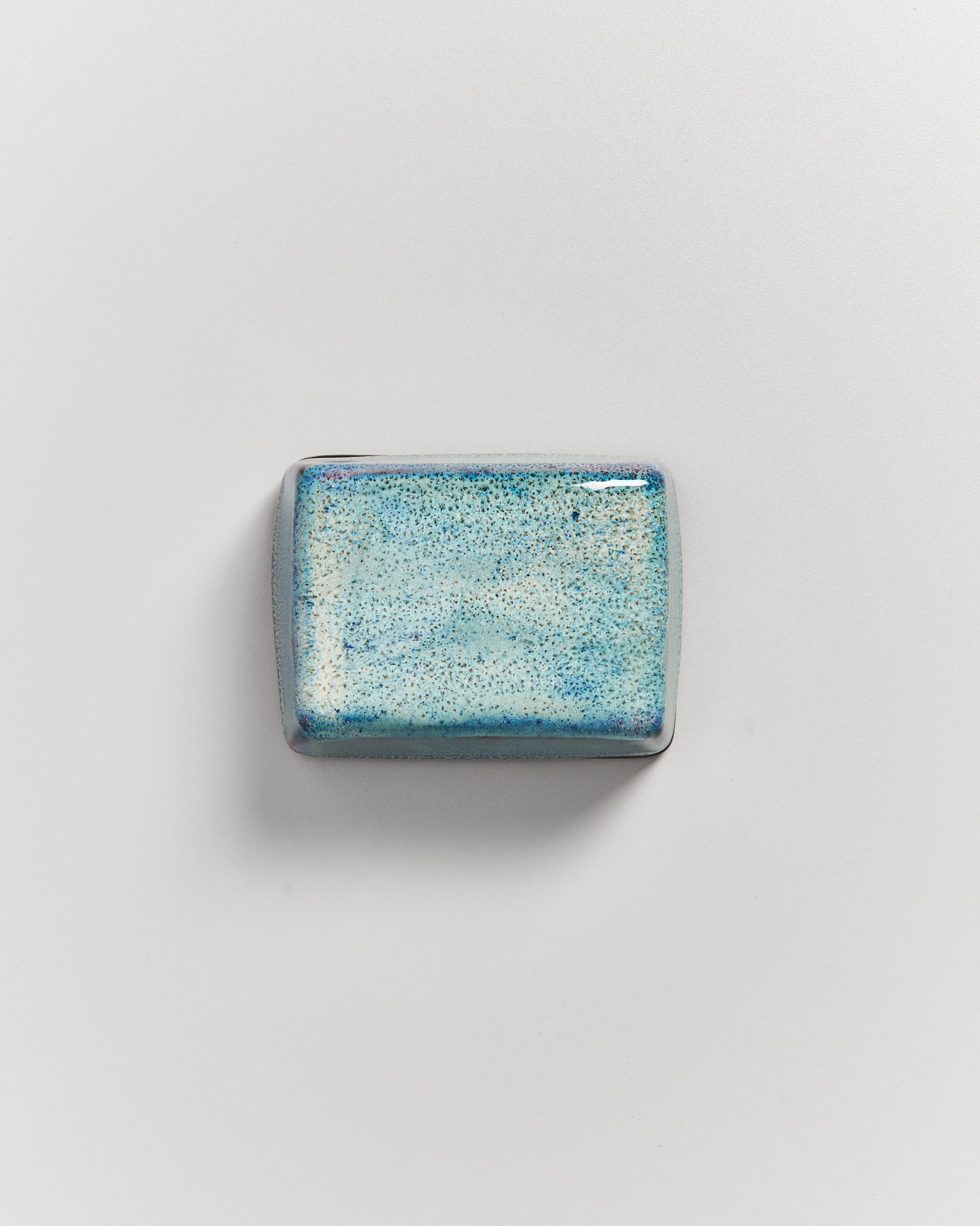 Rechteckige, glasierte Keramikkachel in Blautönen auf einer weißen Oberfläche.