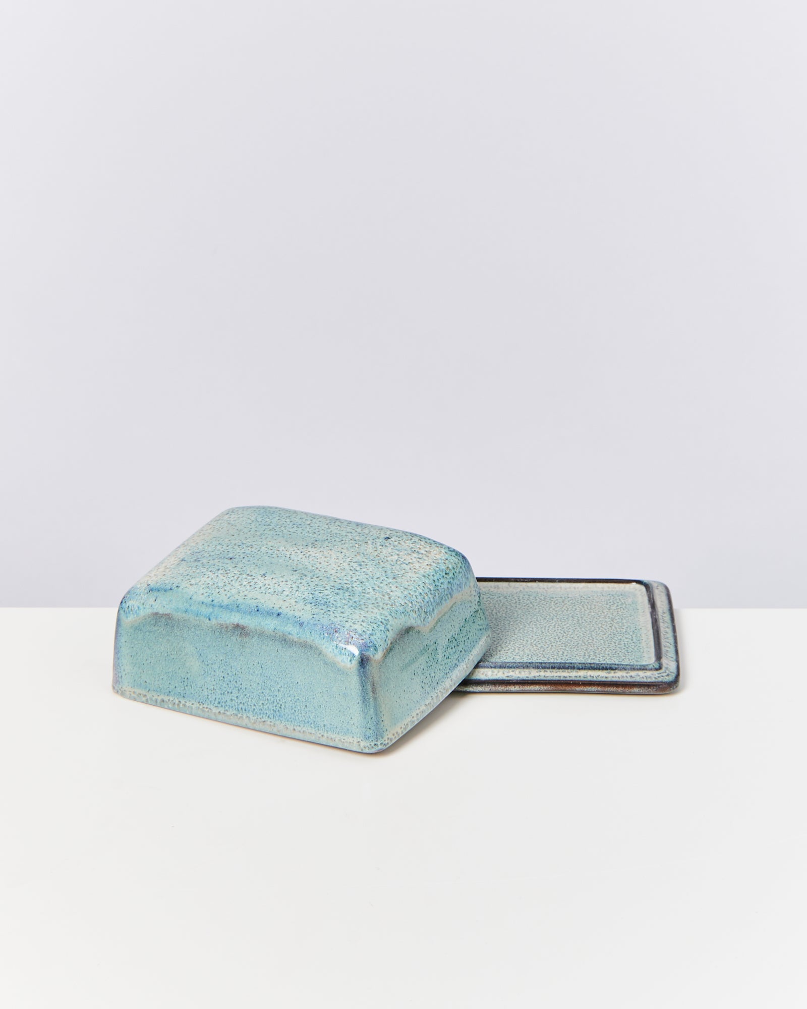 Blaue Keramik-Butterdose mit Deckel und Untertasse auf weißem Hintergrund.