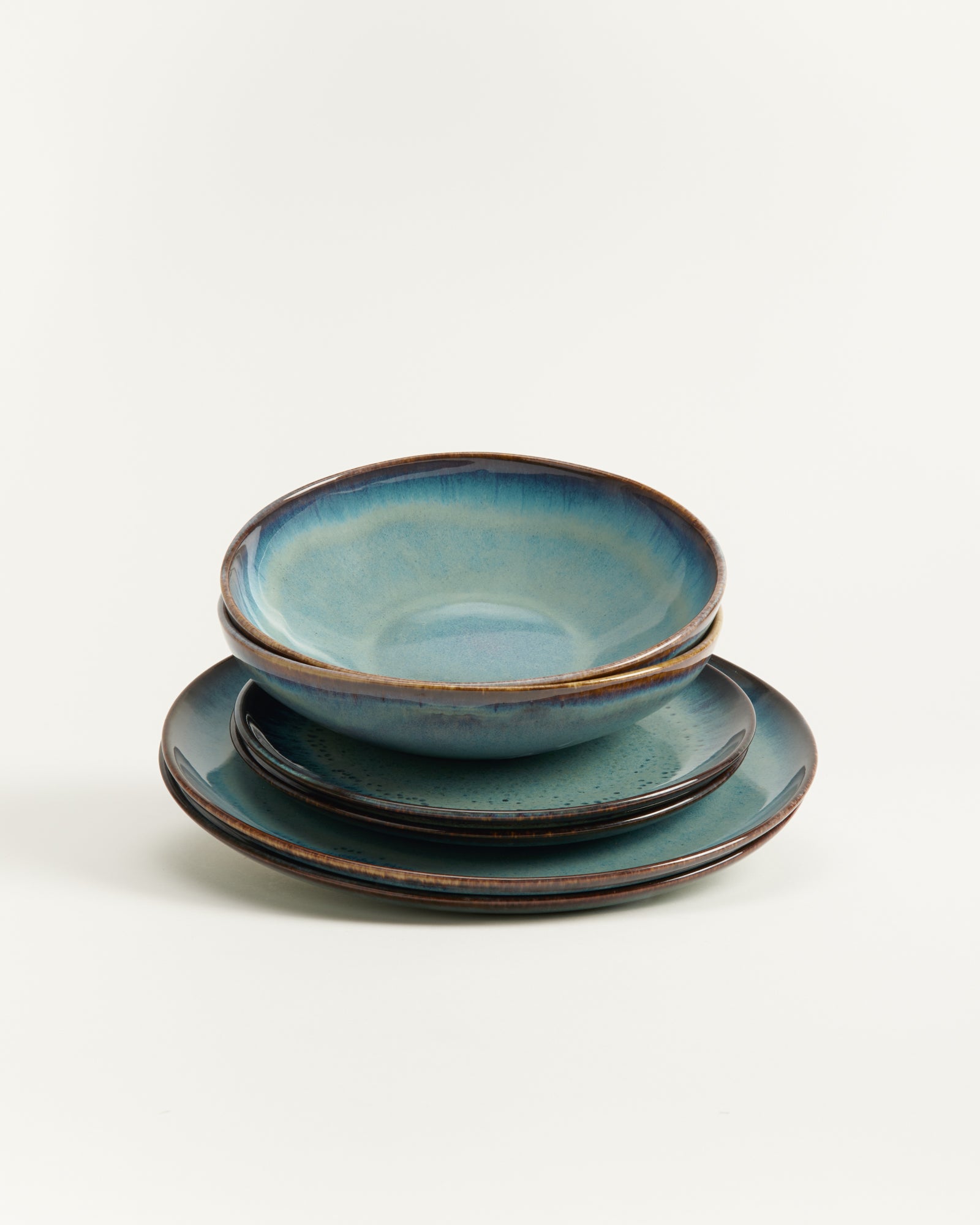 Ein gestapeltes Set aus drei blauen Keramiktellern und einer Schale auf weißem Hintergrund.