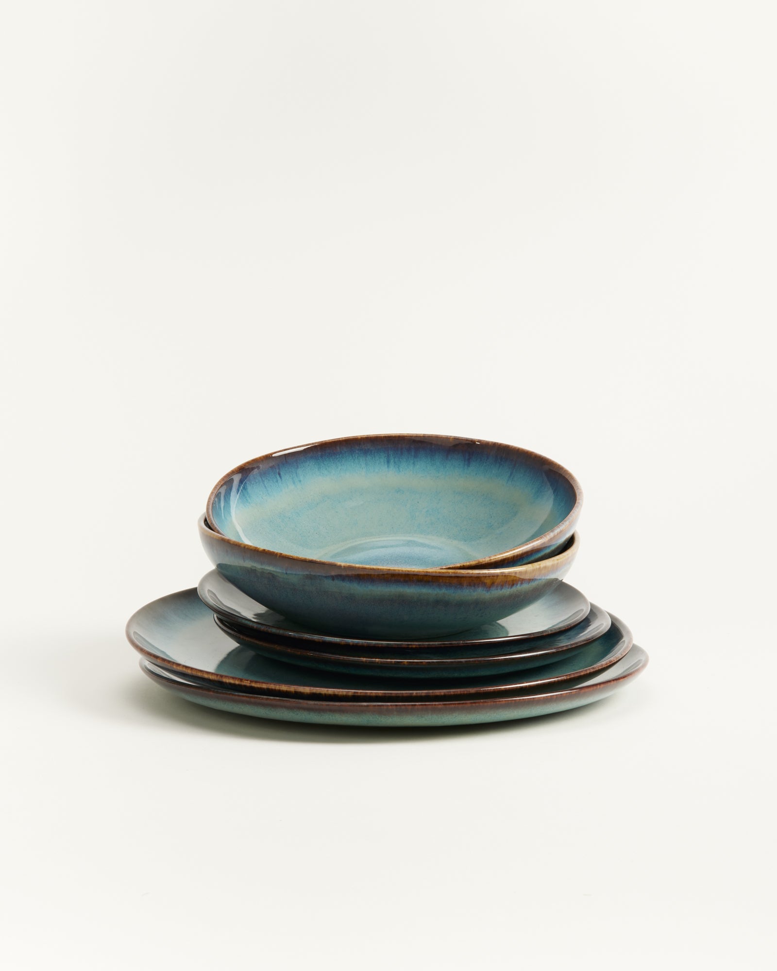 Ein Stapel blau-grüner Keramikteller, lose aufeinander gestapelt auf weißem Hintergrund.