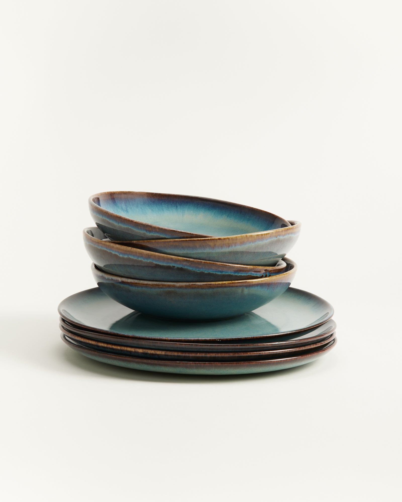 Ein Stapel von vier blauen Keramikschalen und vier Tellern auf weißem Hintergrund.