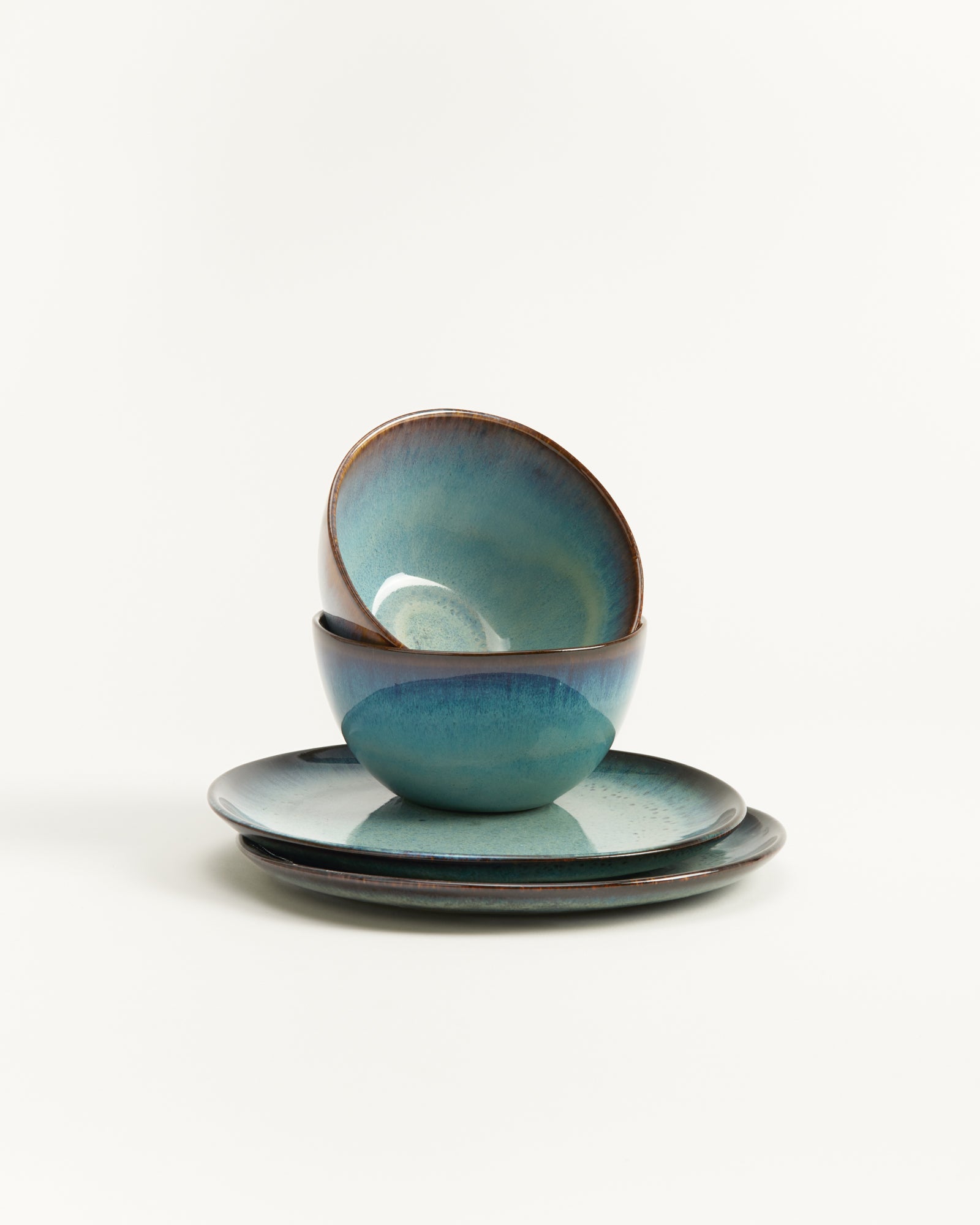 Keramikschalen und -teller in Blau- und Grüntönen gestapelt auf weißem Hintergrund.