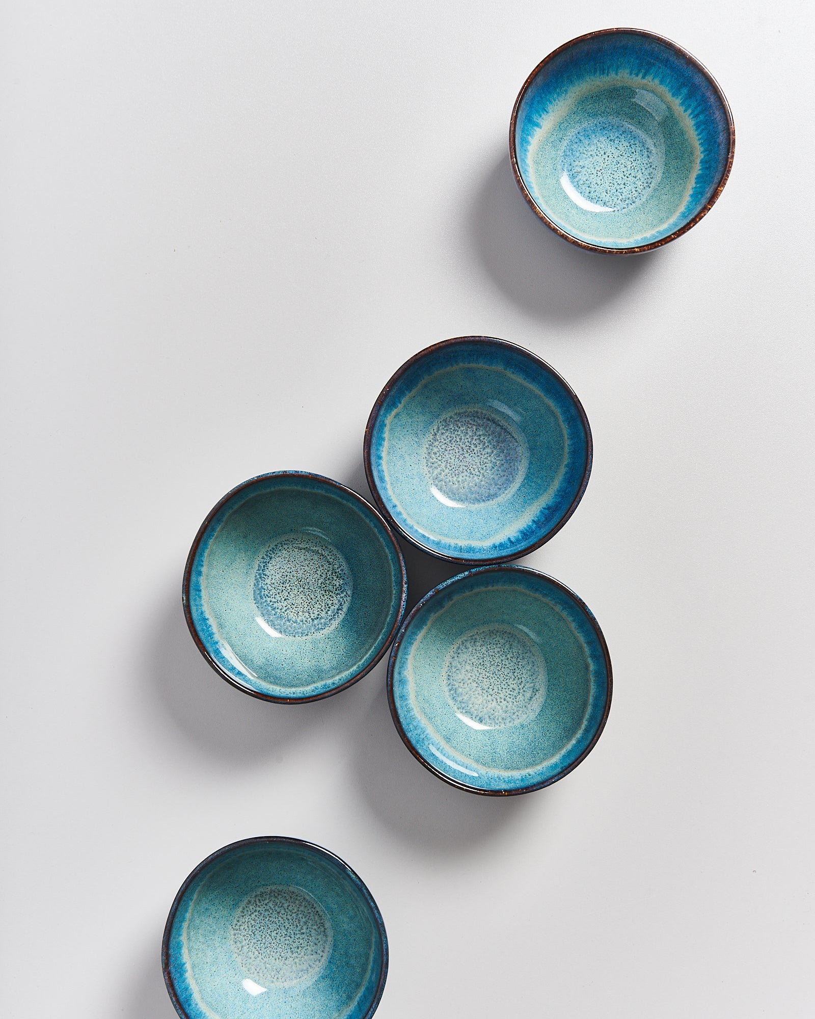 Fünf blaue Keramikschalen mit dunklem Rand auf weißem Hintergrund angeordnet.