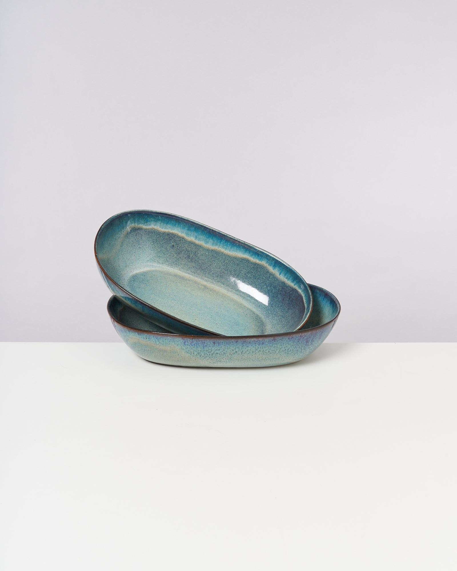 Zwei türkisfarbene, ovale Keramikteller mit leicht glasiertem Finish stehen auf einem weißen Untergrund.