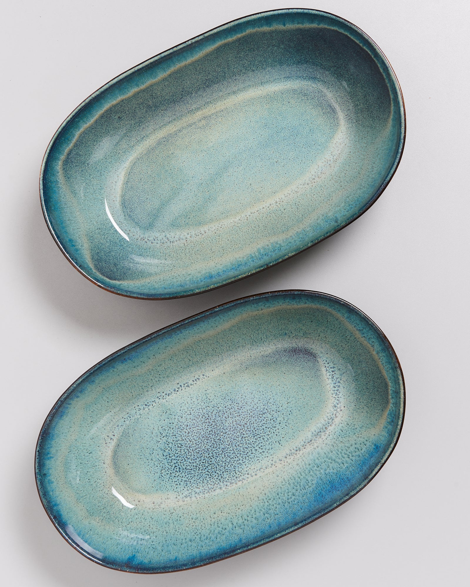 Zwei ovale Teller in Blau- und Grüntönen mit leichtem Farbverlauf liegen auf einer hellen Oberfläche.