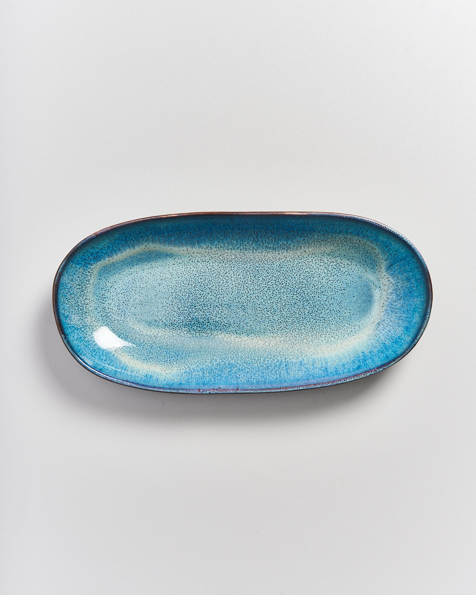 Ovaler, blauer Keramikteller mit leicht gesprenkeltem Muster auf einer weißen Oberfläche.