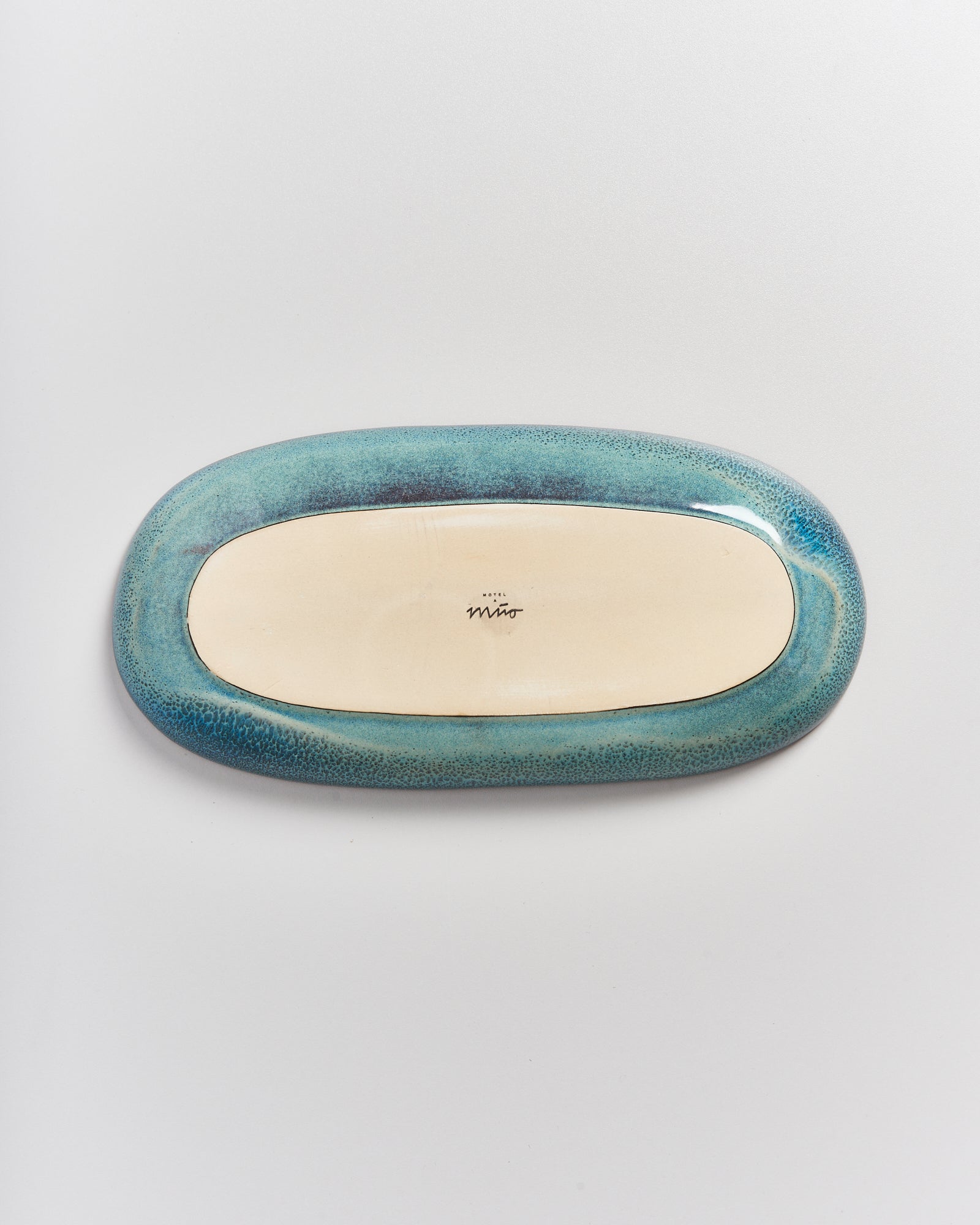 Ovale Keramikplatte mit türkisfarbenem Rand und einer Signatur in der Mitte auf der Unterseite.