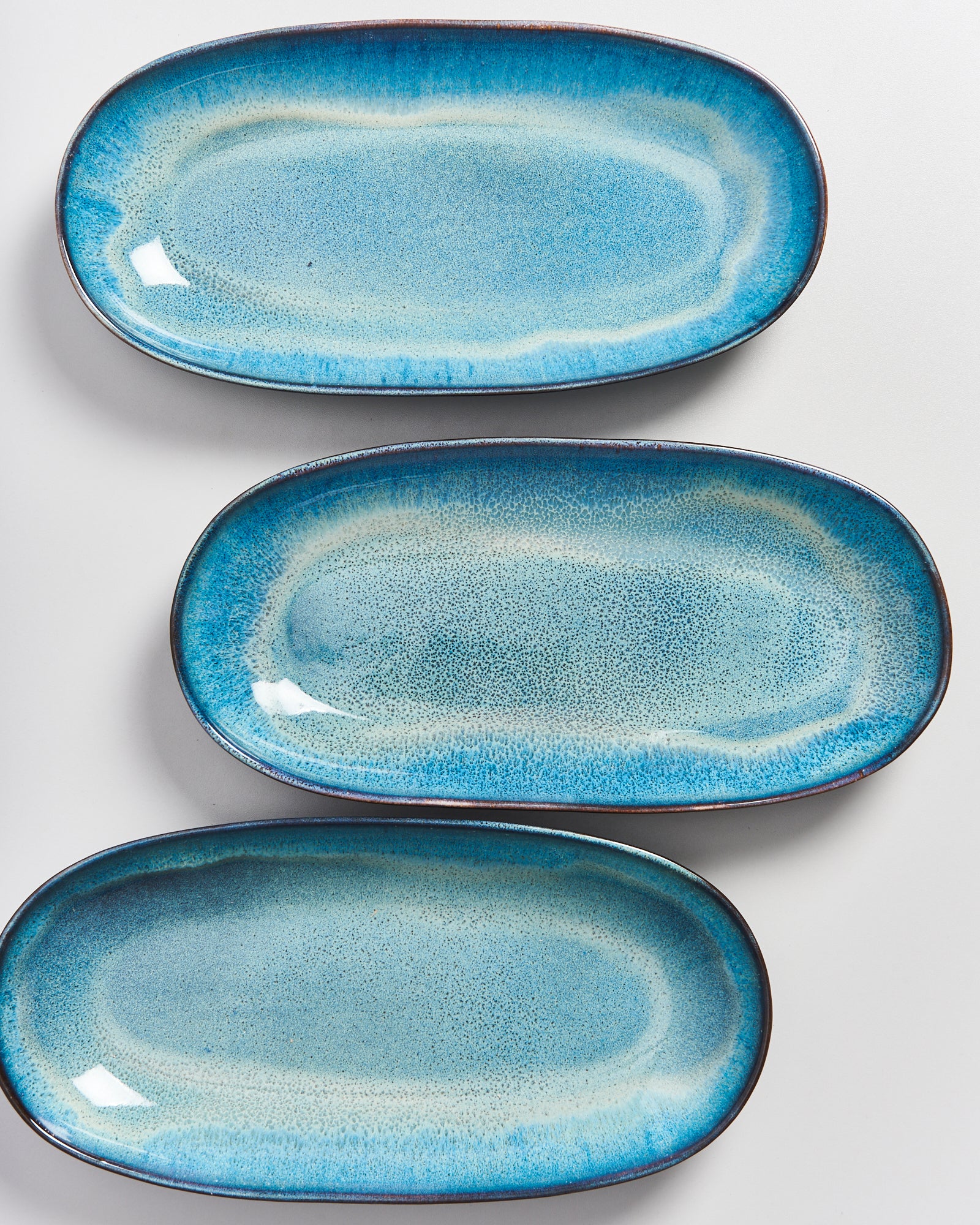 Drei ovale, blaue Keramikteller mit gewelltem Rand auf einer weißen Oberfläche.
