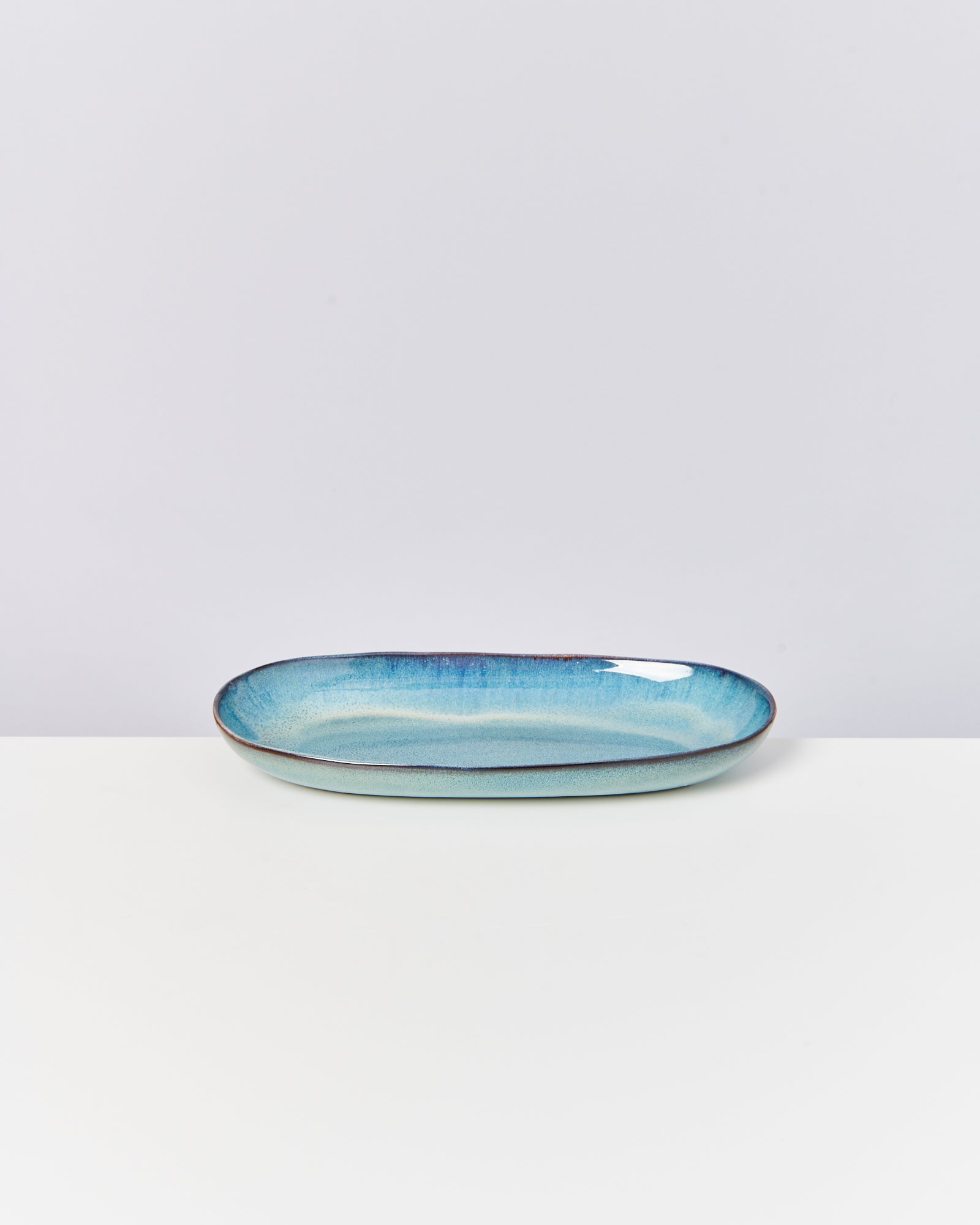 Blaue ovale Keramikschale auf einer weißen Oberfläche vor einem hellgrauen Hintergrund.