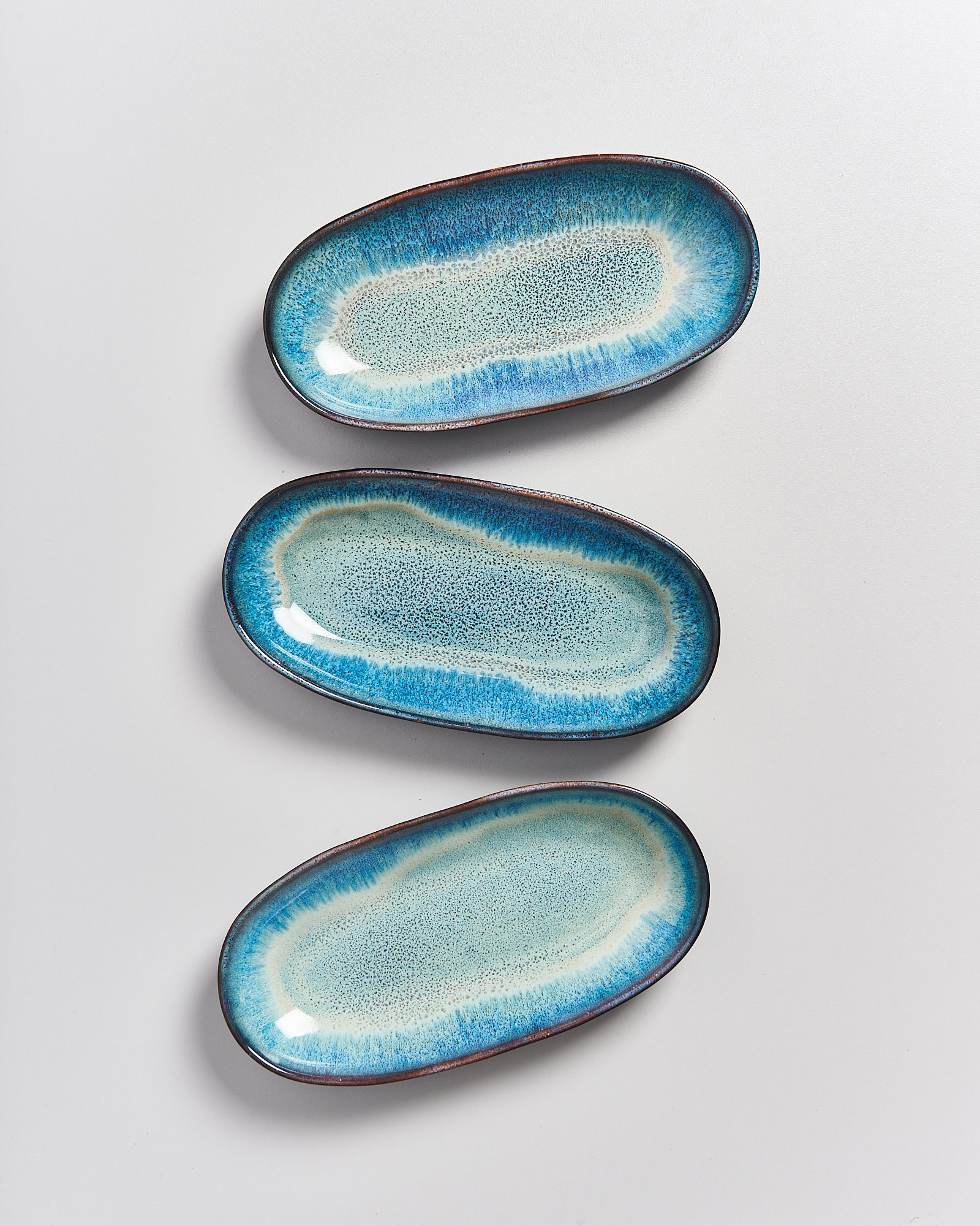 Drei ovale, blau-grün glasierte Keramikteller auf einem weißen Hintergrund.