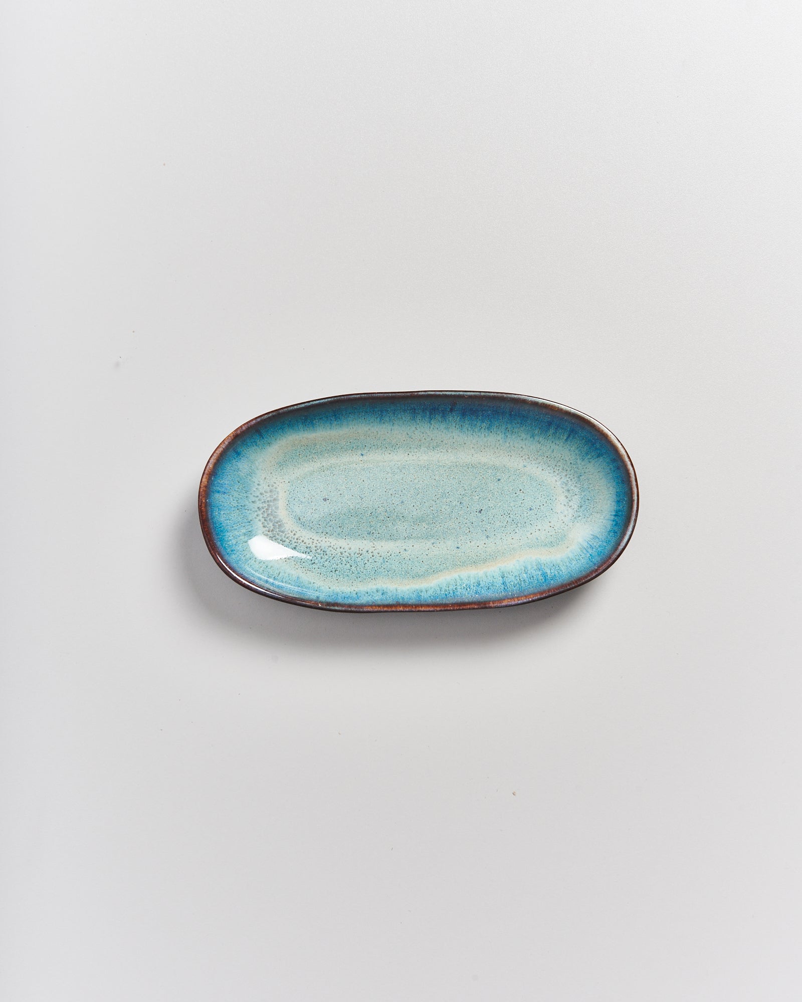 Türkisblauer, ovaler Keramikteller mit dunkelbraunem Rand, auf weißem Hintergrund.