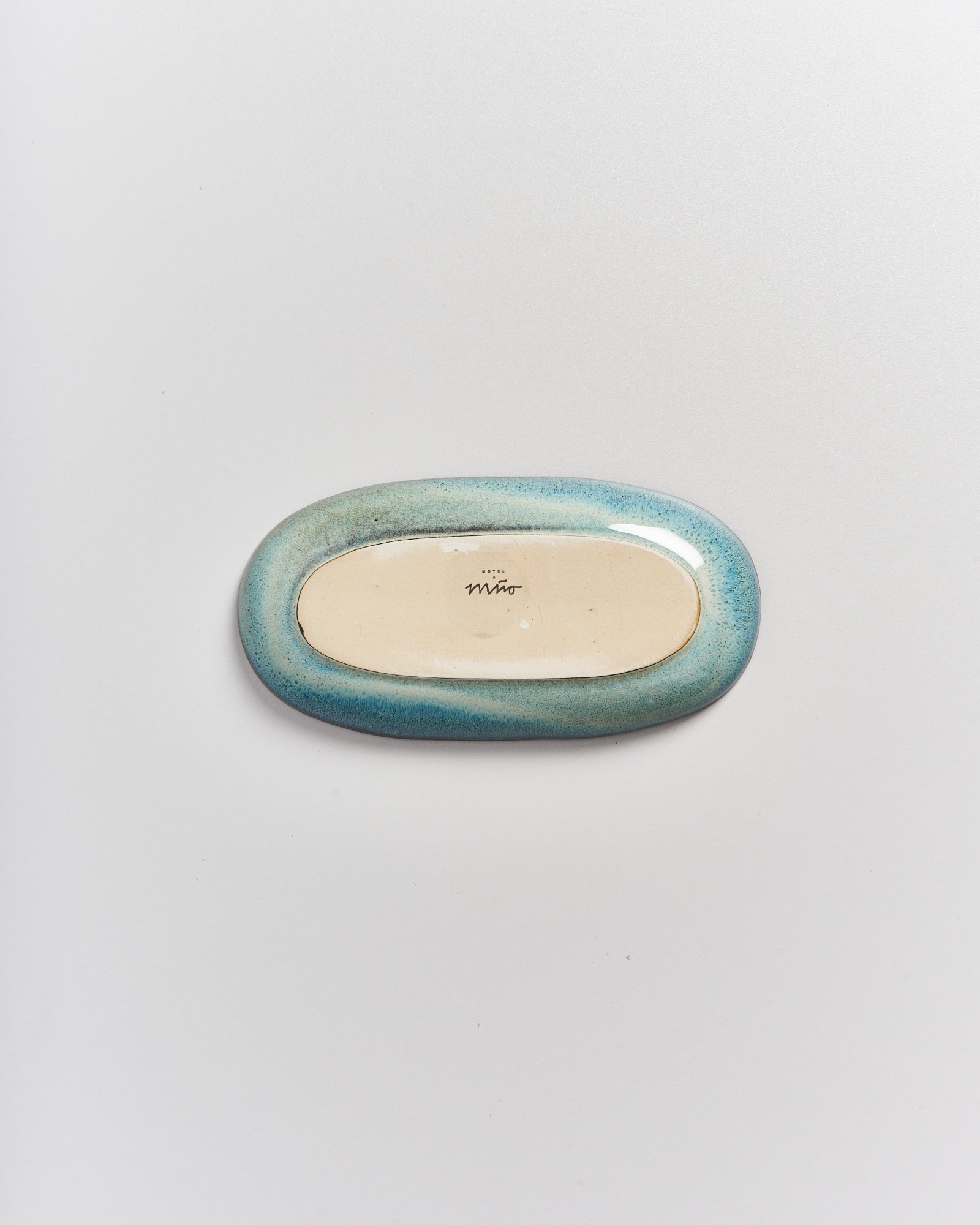 Ovaler Keramikgegenstand mit blauem Rand und beiger Mitte, auf einer weißen Oberfläche positioniert.