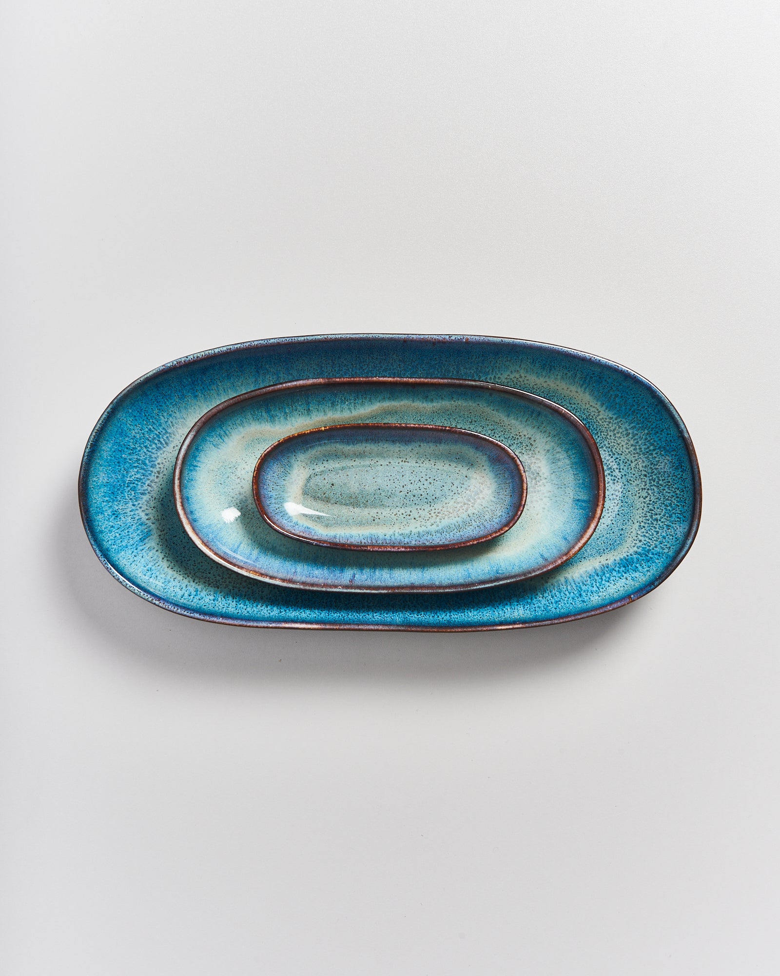 Drei geschichtete, ovale, türkisfarbene Keramikteller auf einer weißen Oberfläche.