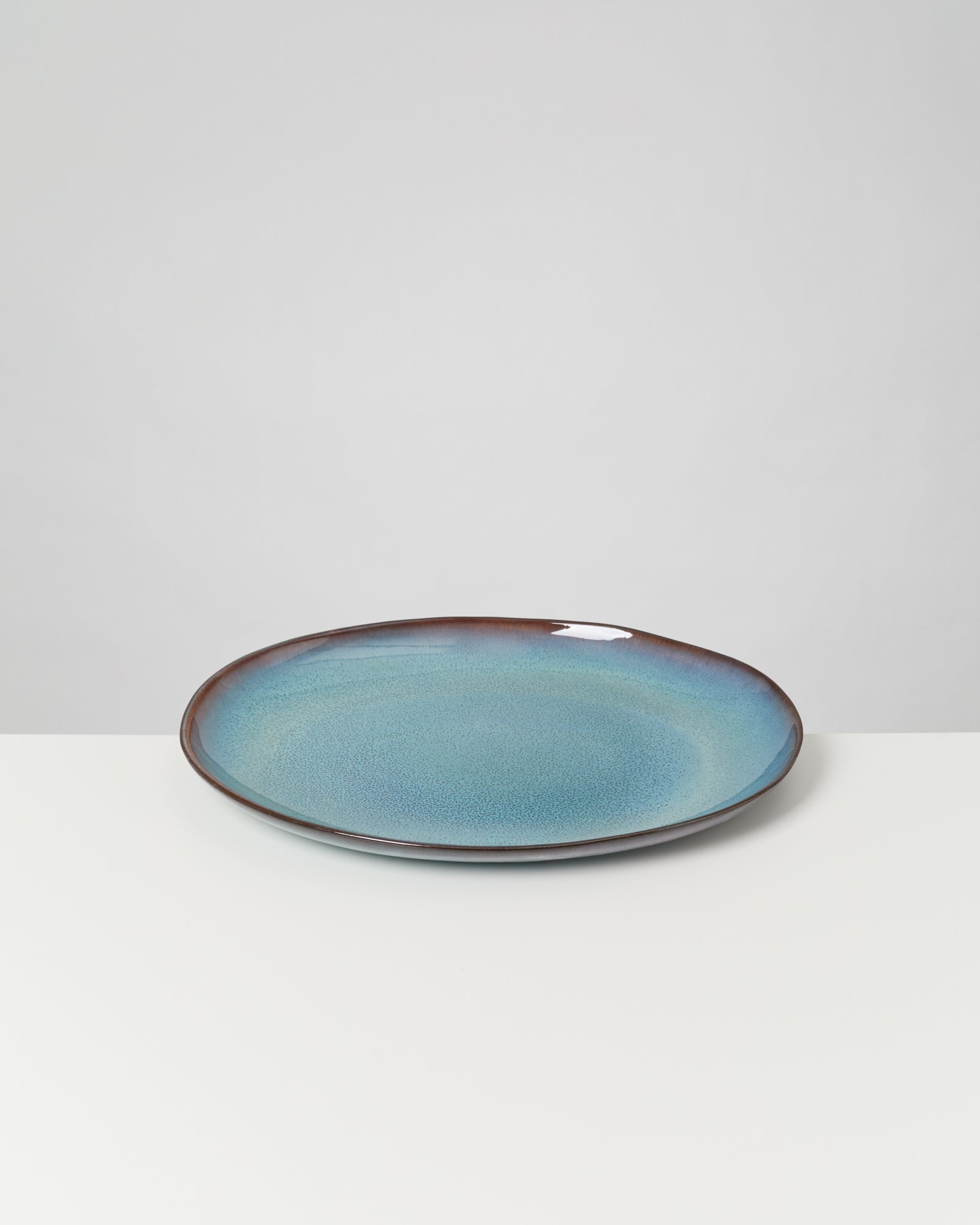 Blauer Keramikteller mit dunkelbraunem Rand auf weißem Hintergrund.