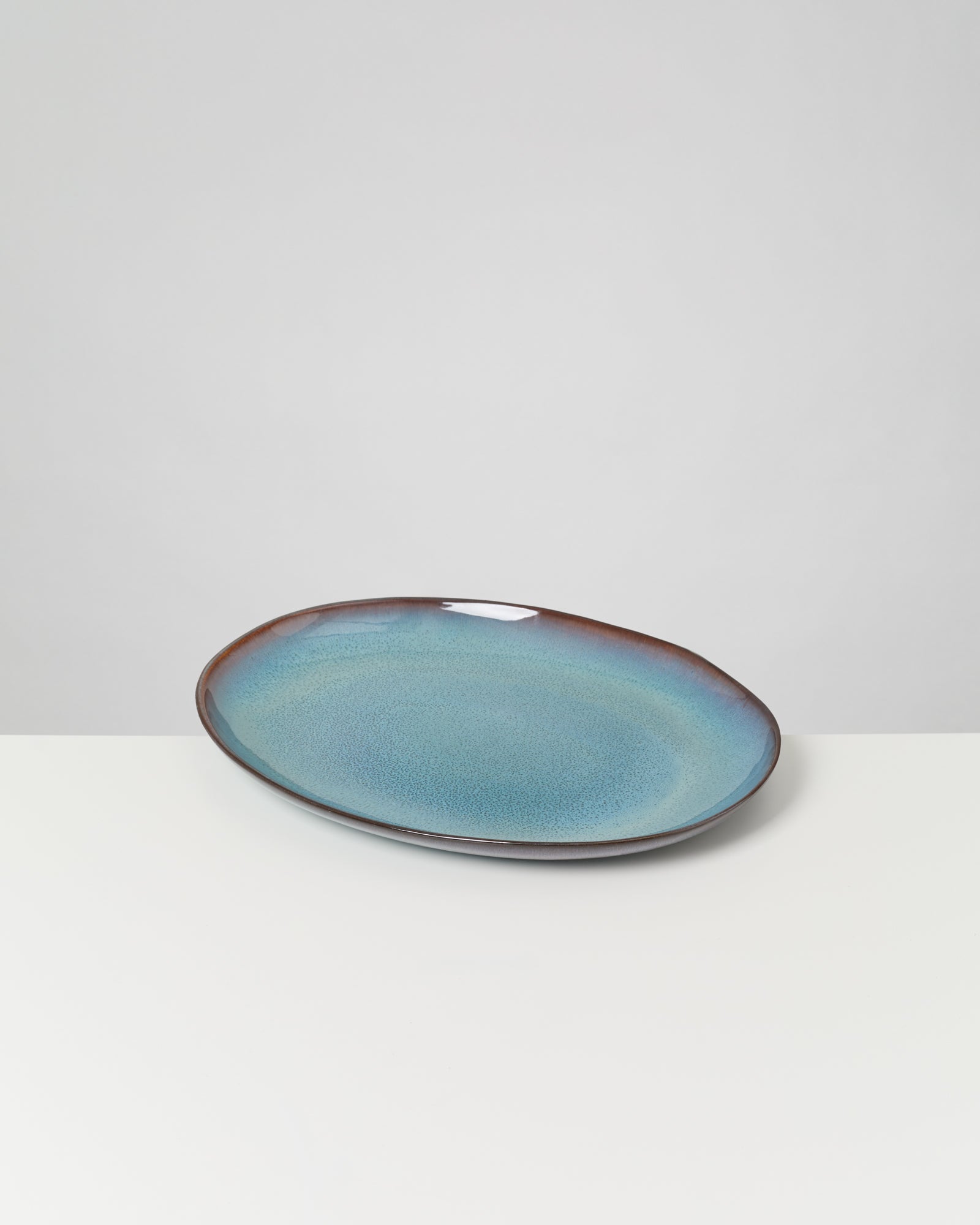 Ovale Platte aus Keramik mit blauem Farbverlauf und glänzender Oberfläche auf einem weißen Hintergrund.