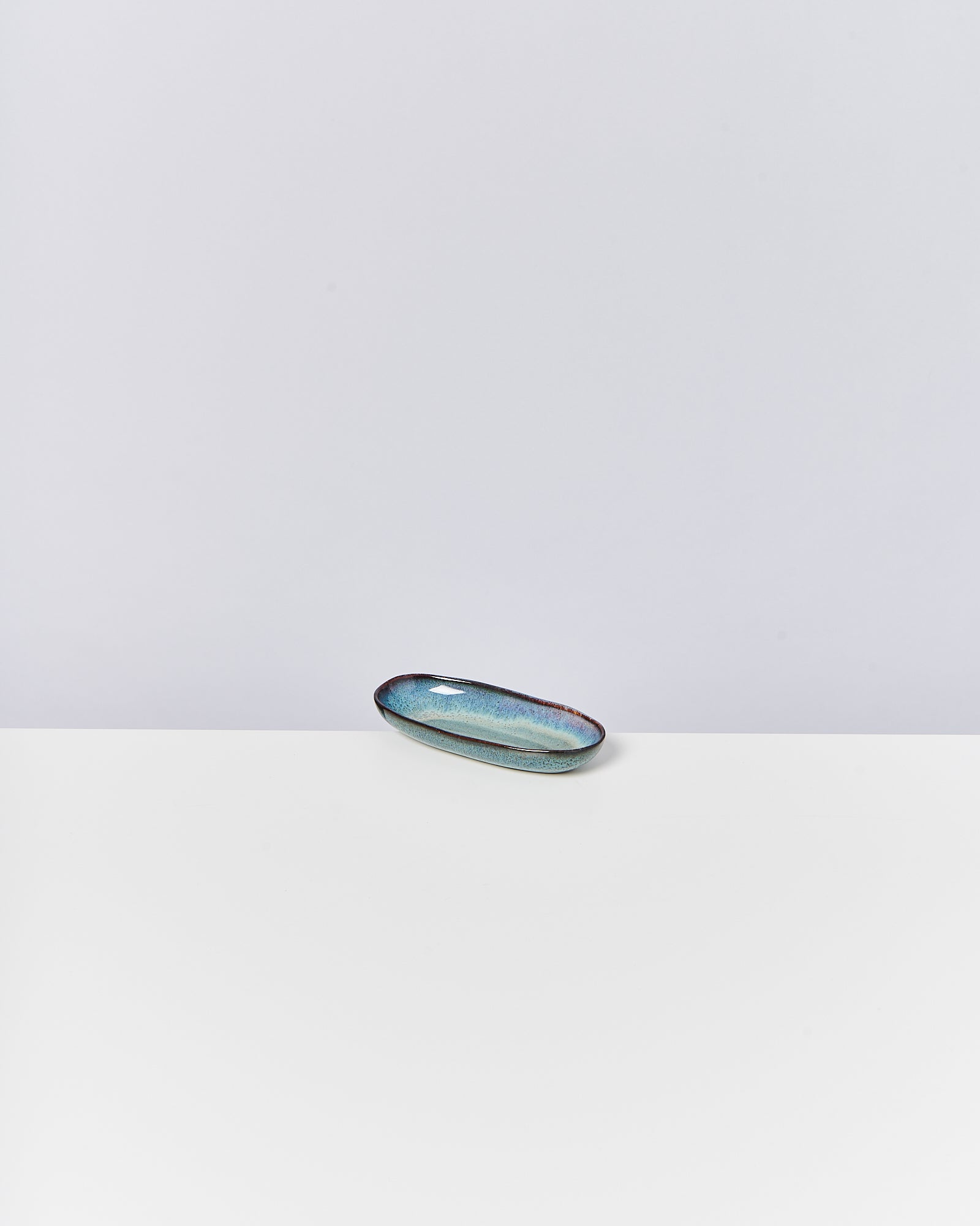 Kleine, längliche Keramikschale mit blau-grüner Glasur auf weißem Hintergrund.