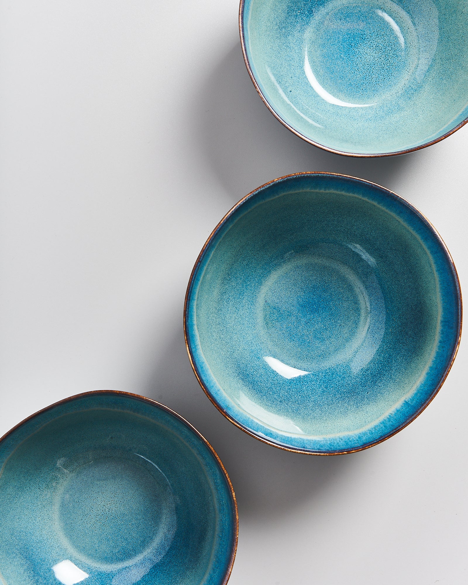 Drei runde, blau-glasierte Schalen liegen diagonal auf einem hellgrauen Hintergrund.