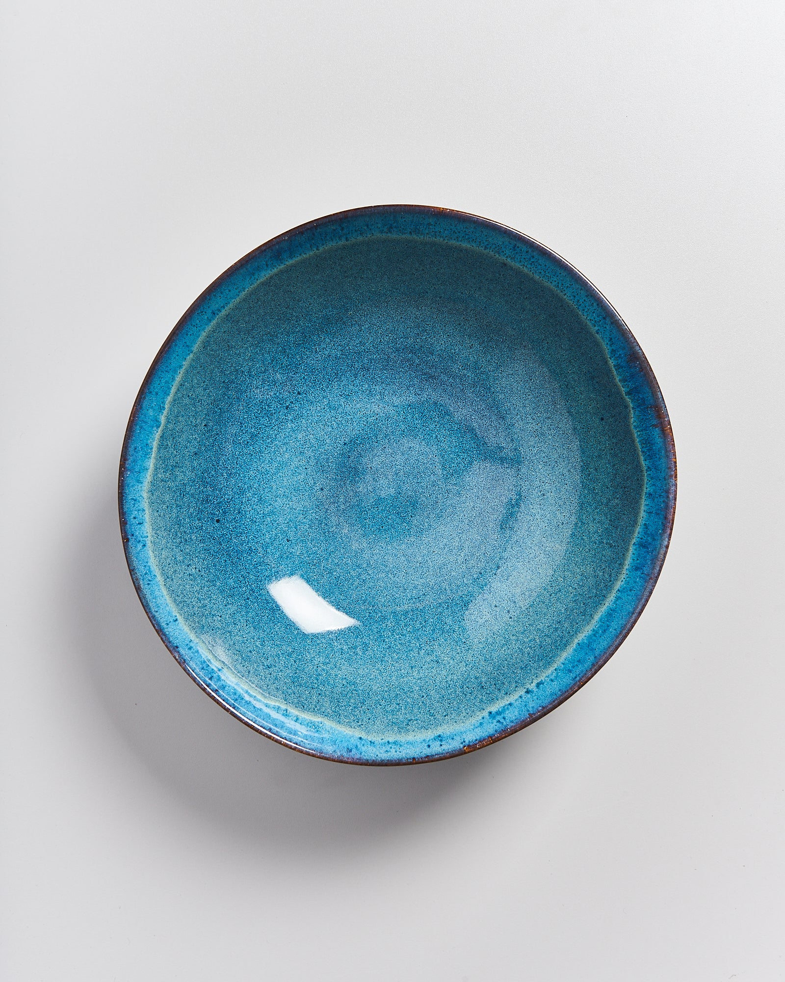 Blaue Keramikschale mit dunklem Rand auf weißem Hintergrund.