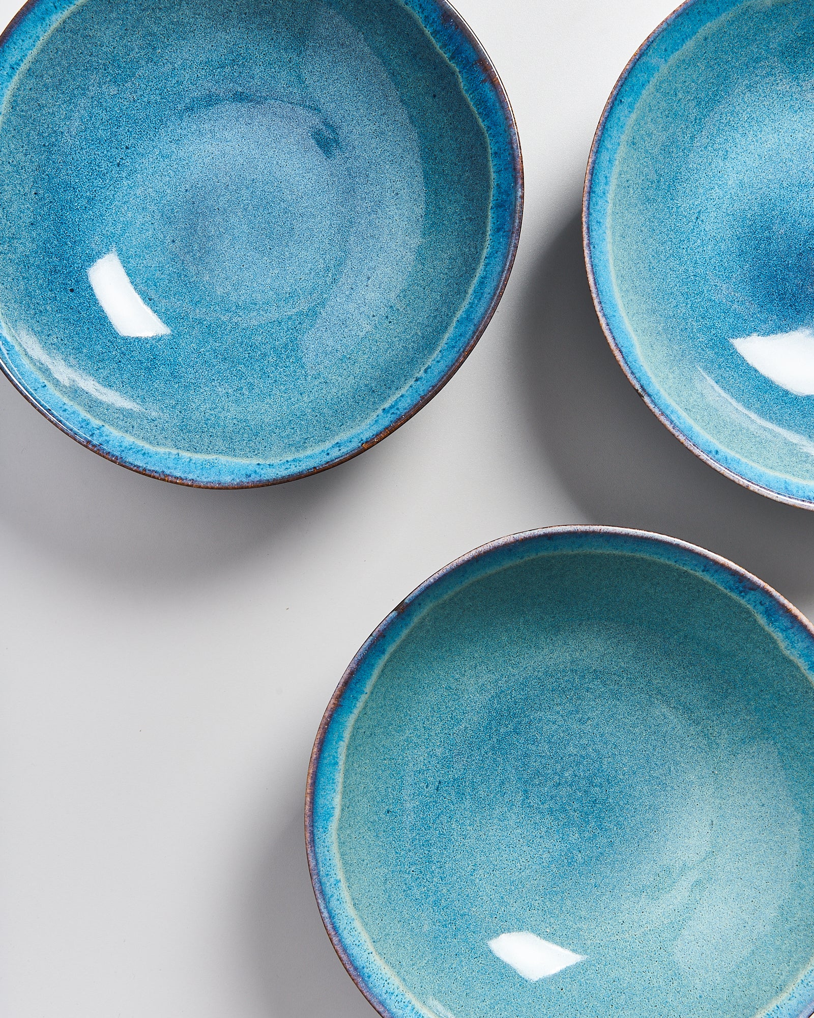 Drei blaue Keramikschüsseln mit glasierten Oberflächen auf einer hellen Hintergrundfläche.