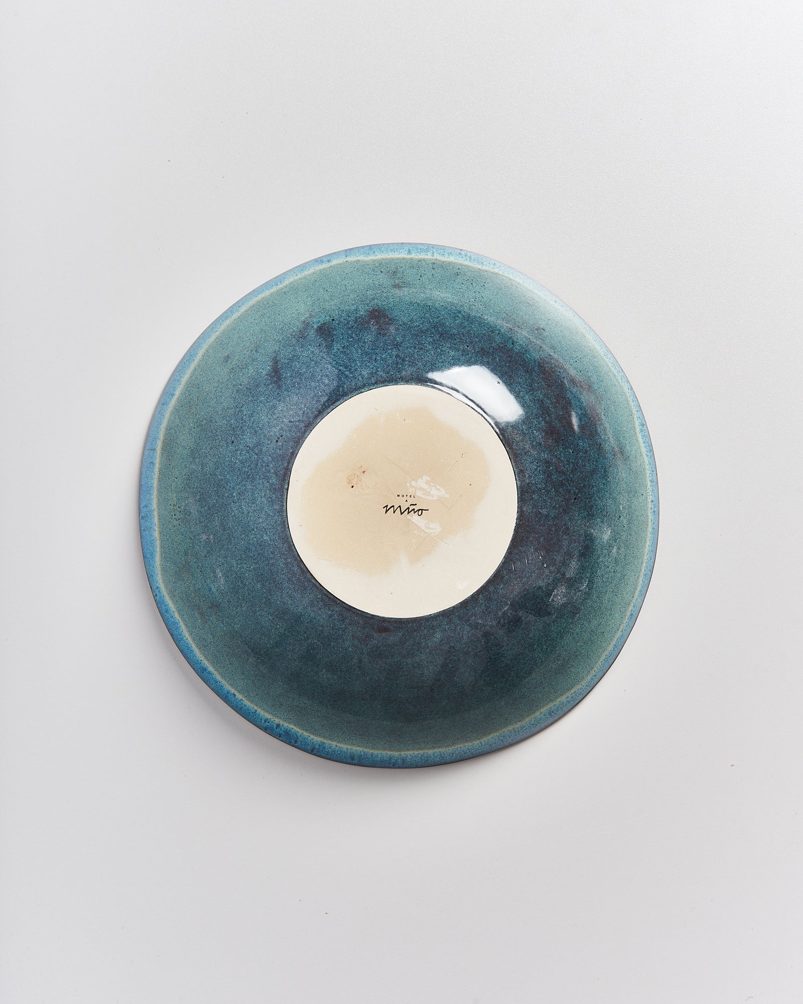 Eine grün-blaue Keramikschale mit hellem Boden und darauf handschriftlichem Schriftzug auf weißem Hintergrund.